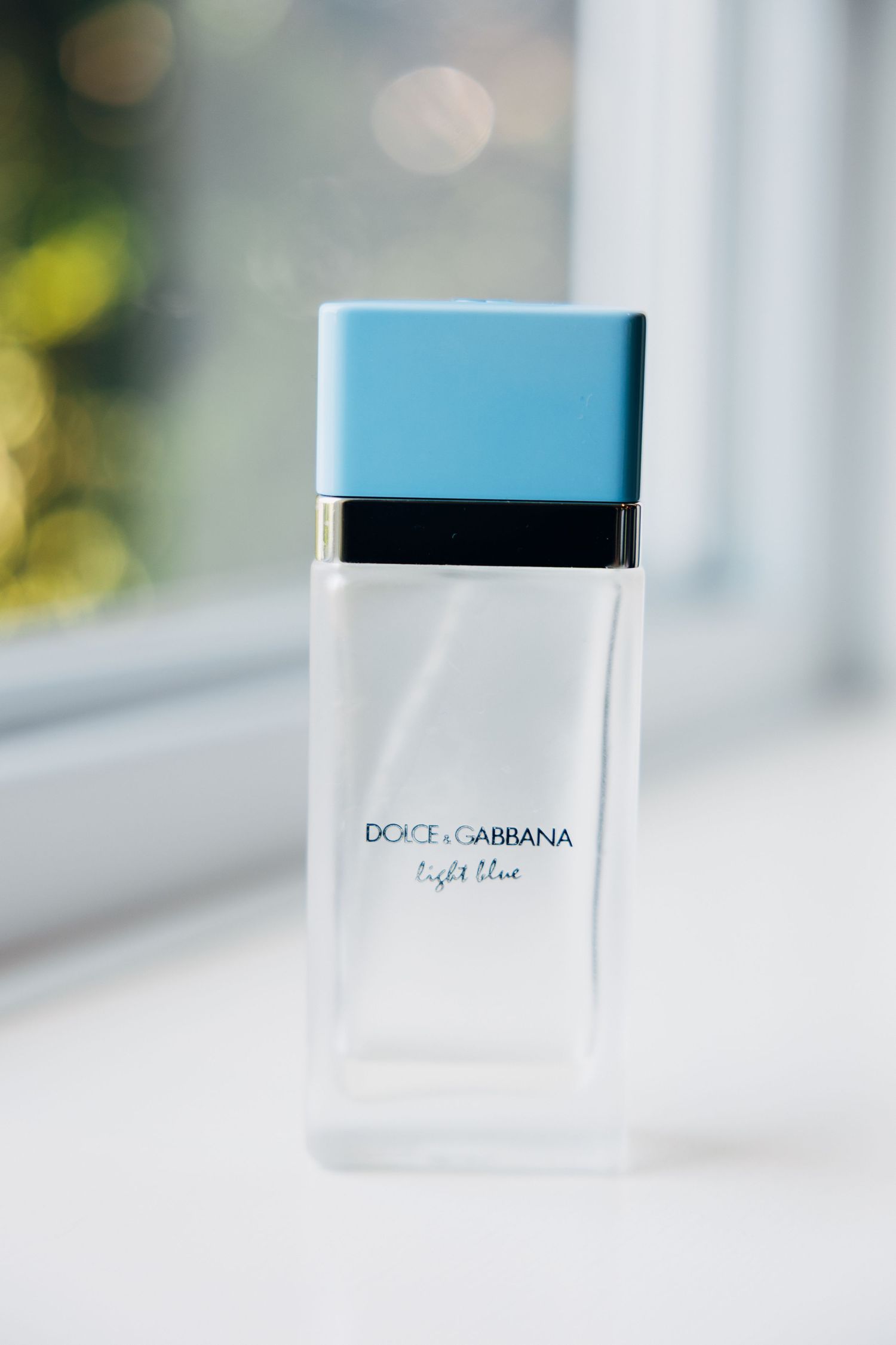 Dolce & Gabbana Light Blue perfume bottle with a light blue cap on a white windowsill.