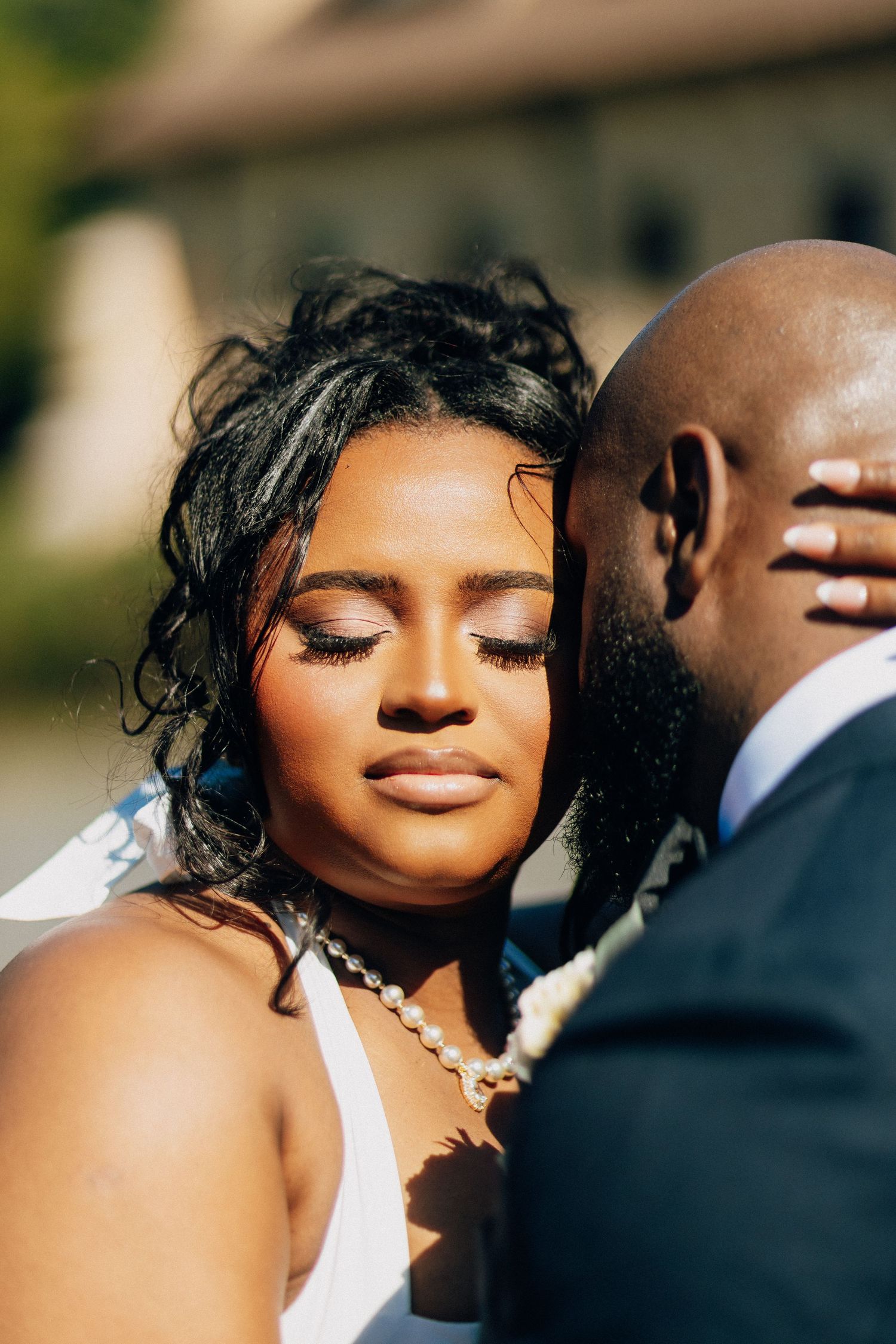Close-up of a beautiful Black bride with elegant makeup and pearl necklace, eyes closed, leaning against groom.