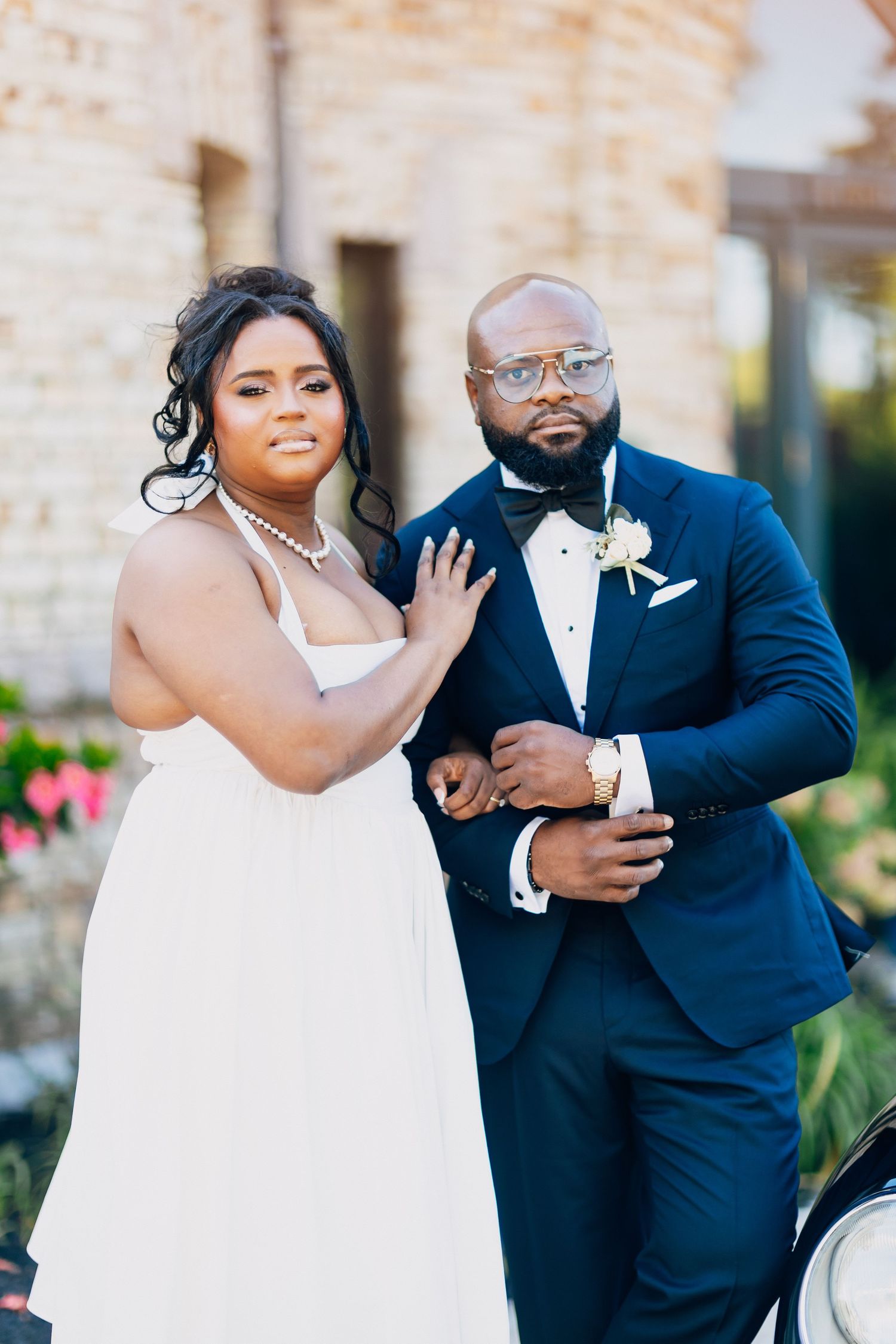 Elegant Black bride in white dress and groom in navy tuxedo posing together outdoors on their wedding day.