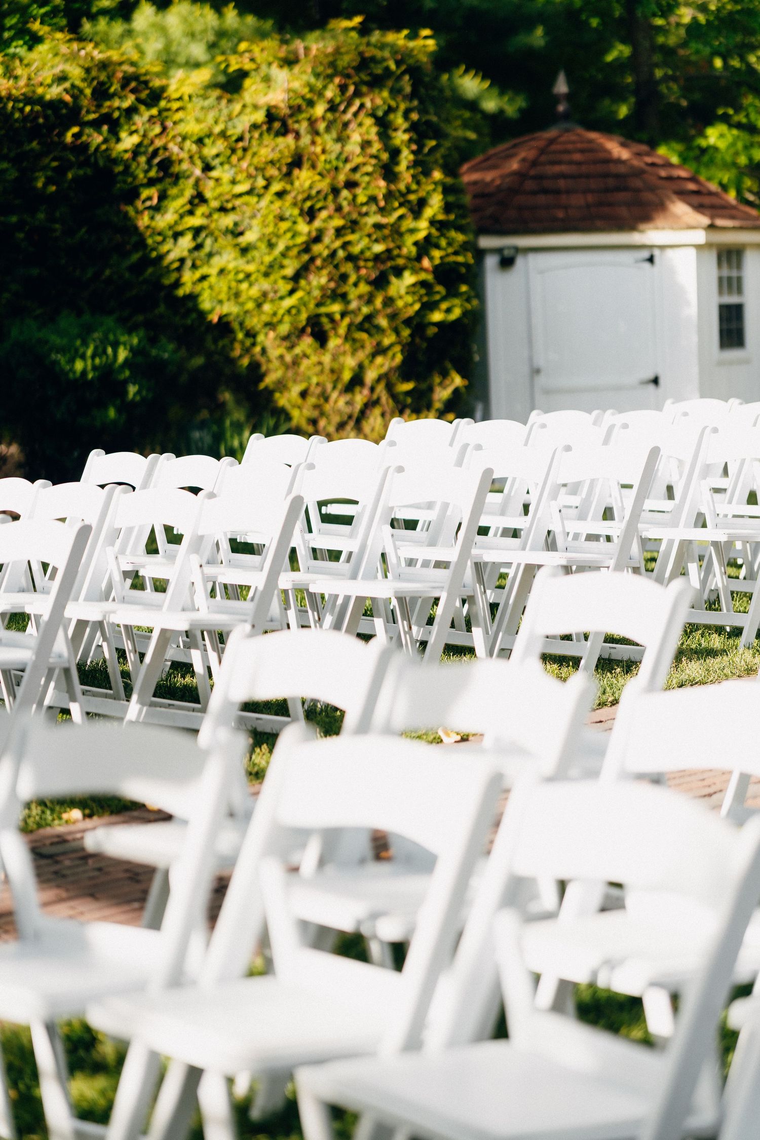 Rows of white folding chairs set up for an outdoor garden wedding ceremony.