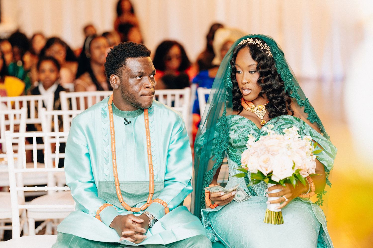 Bride and groom in matching teal African traditional attire sit together at wedding.