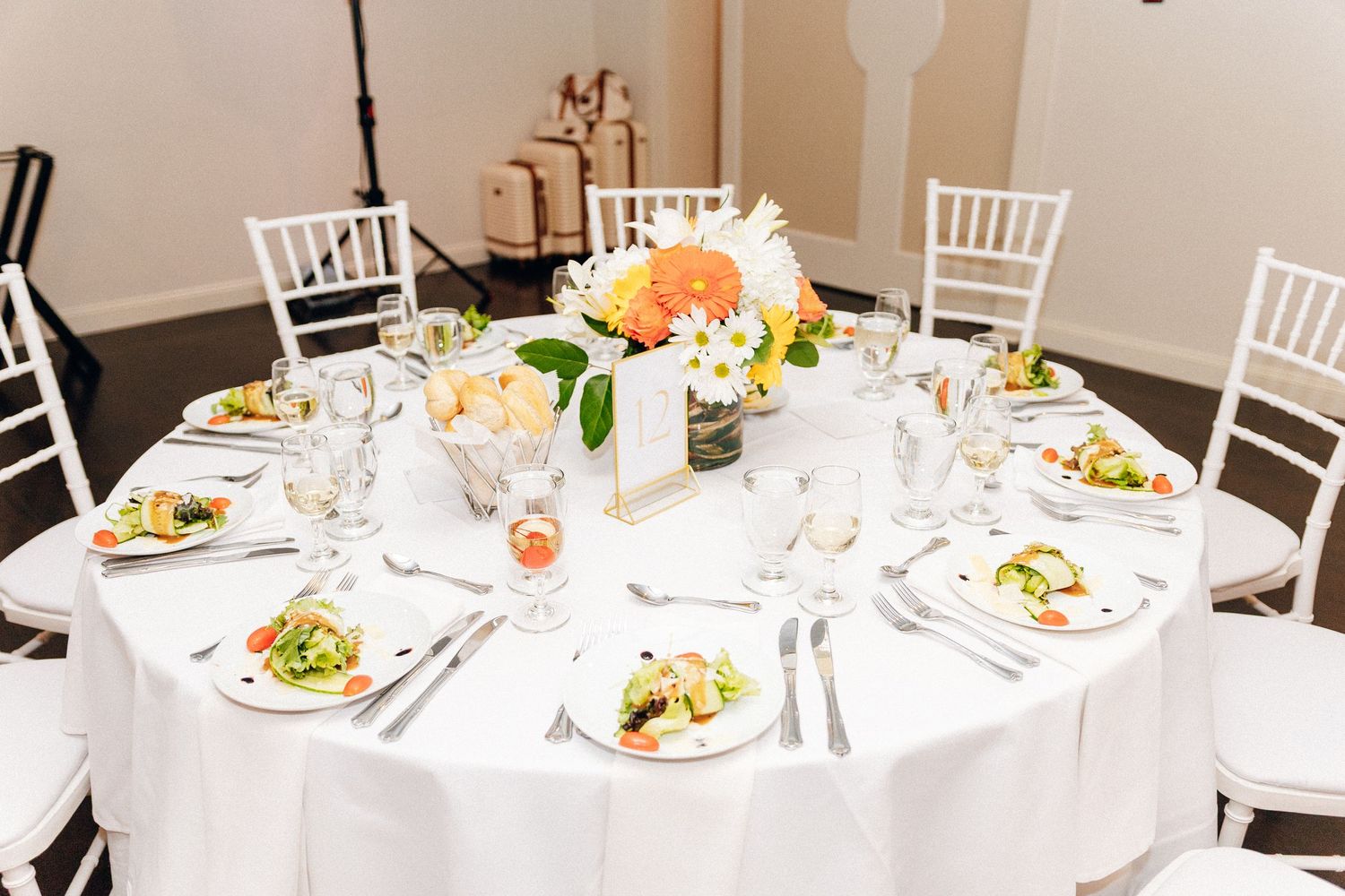 Elegant wedding reception table with white linen, white chairs, and a vibrant orange and white floral centerpiece.
