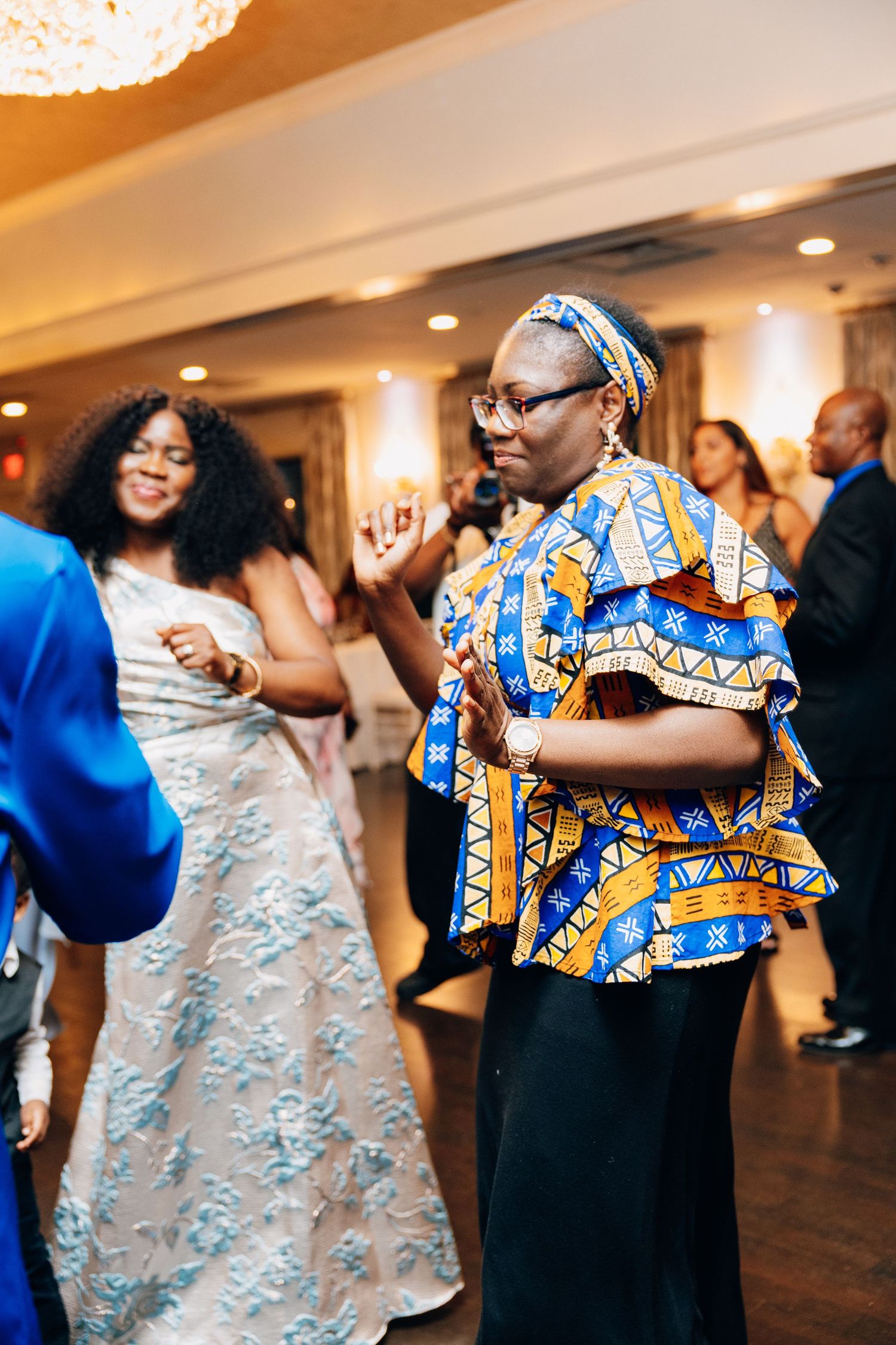 Guests dancing joyfully at a wedding reception, woman in colorful African print top enjoying the celebration.