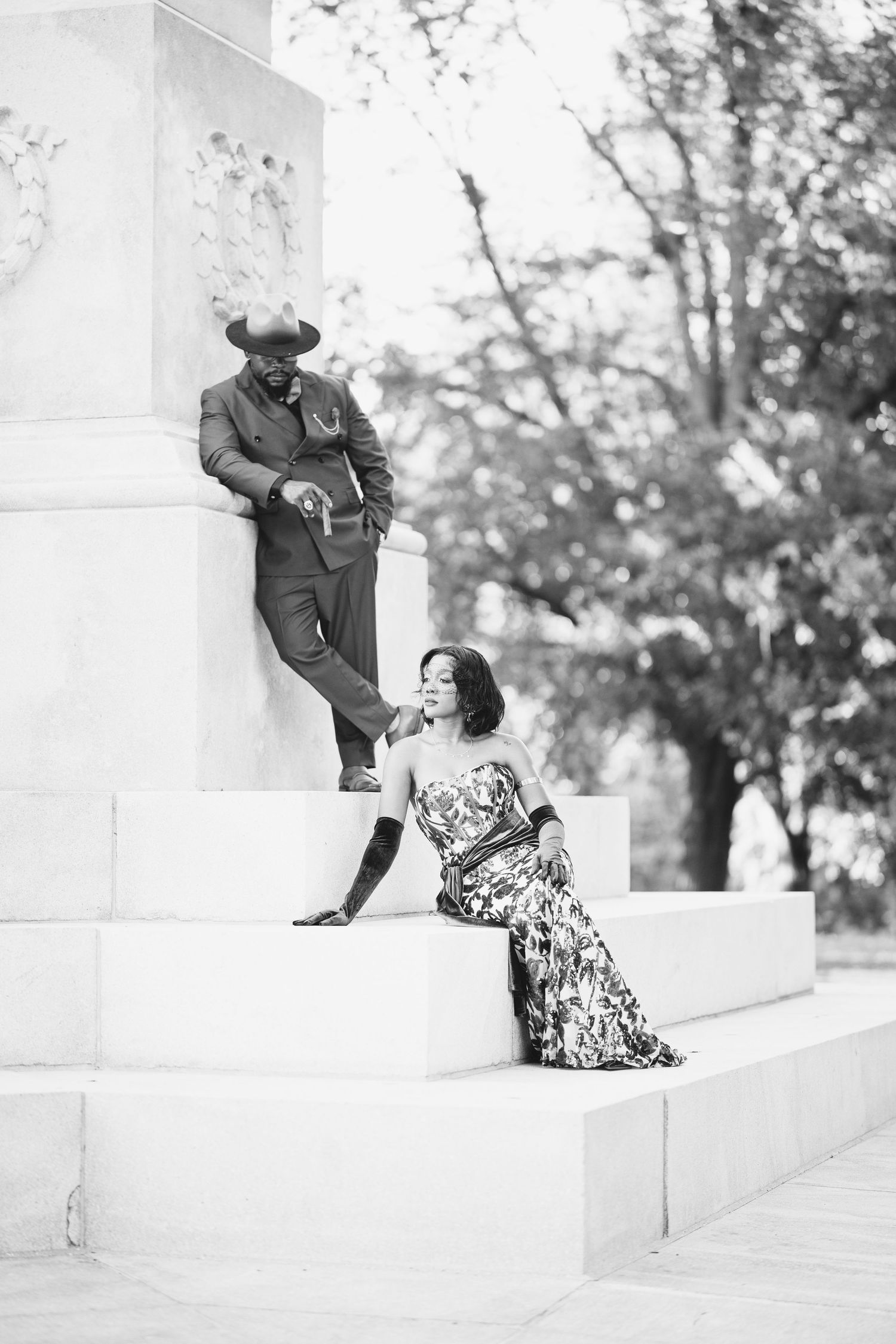 Black and white photo of a couple posing on monument steps in formal attire.