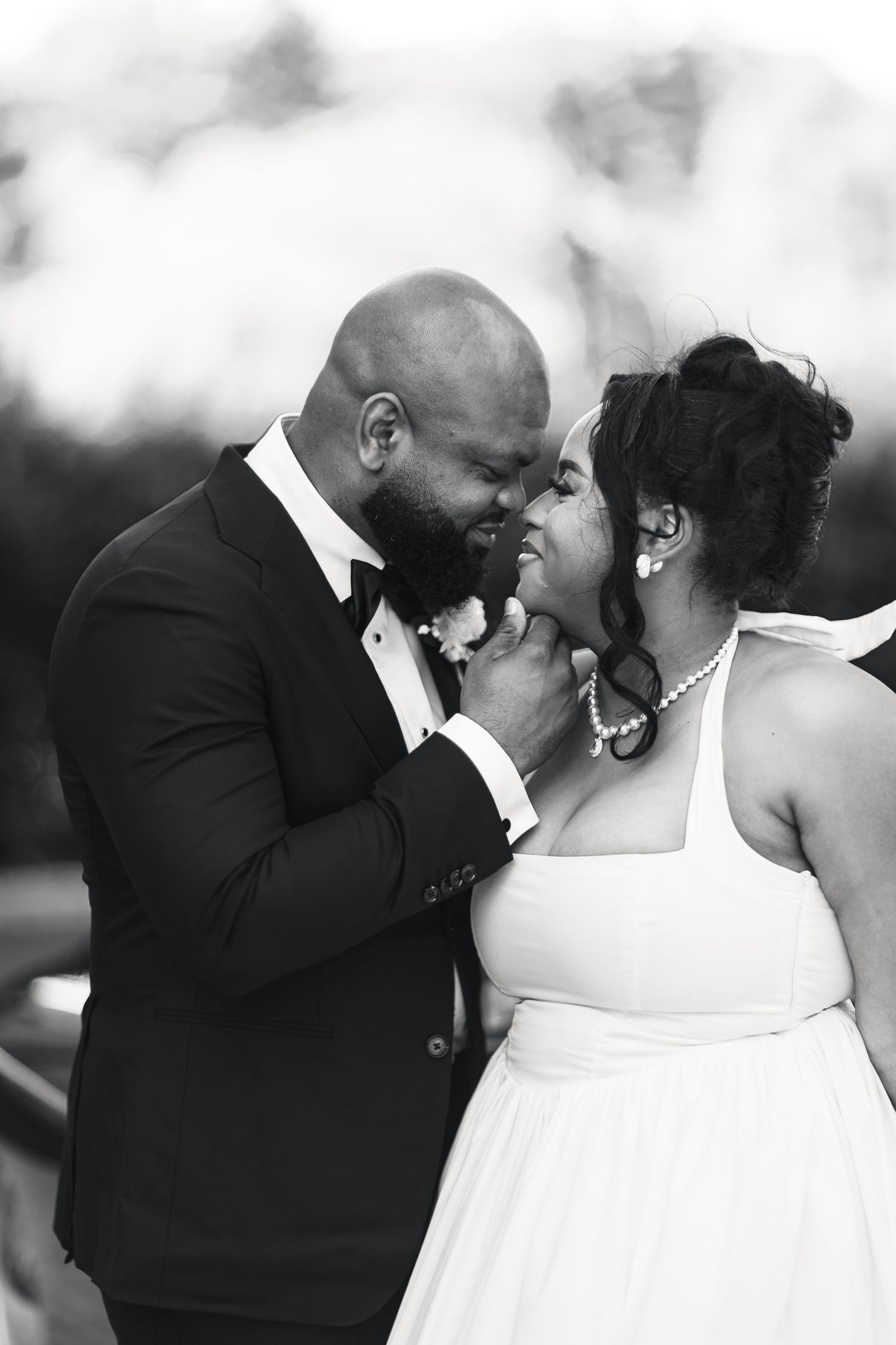 Black and white romantic portrait of bride and groom nearly kissing at outdoor wedding.