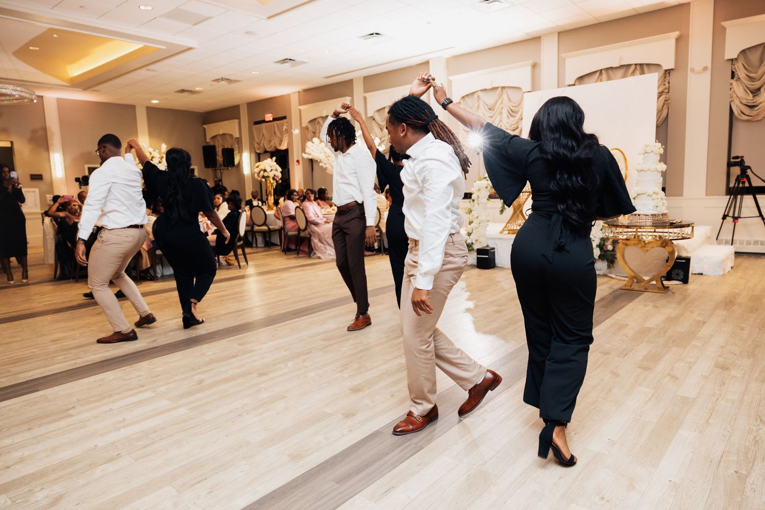 Guests dancing joyfully at an elegant wedding reception in a decorated ballroom with white floral arrangements.