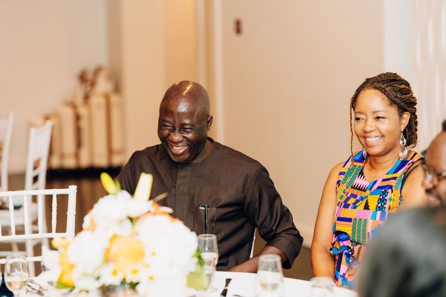 Two guests smiling and laughing at a wedding reception table with floral centerpieces in a elegant venue.
