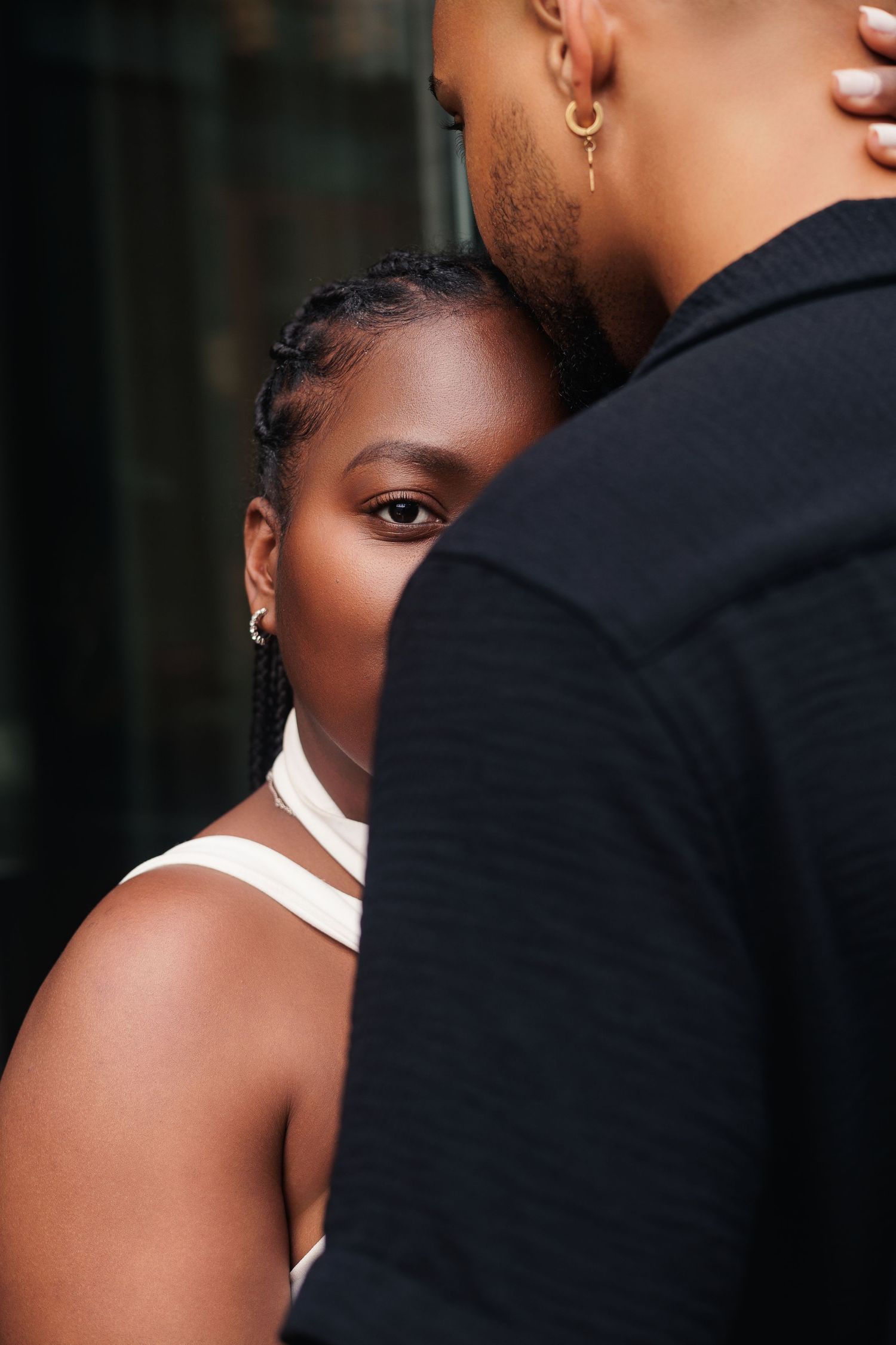 A young Black woman rests her head against a man in a black jacket, gazing at the camera in a close romantic portrait.