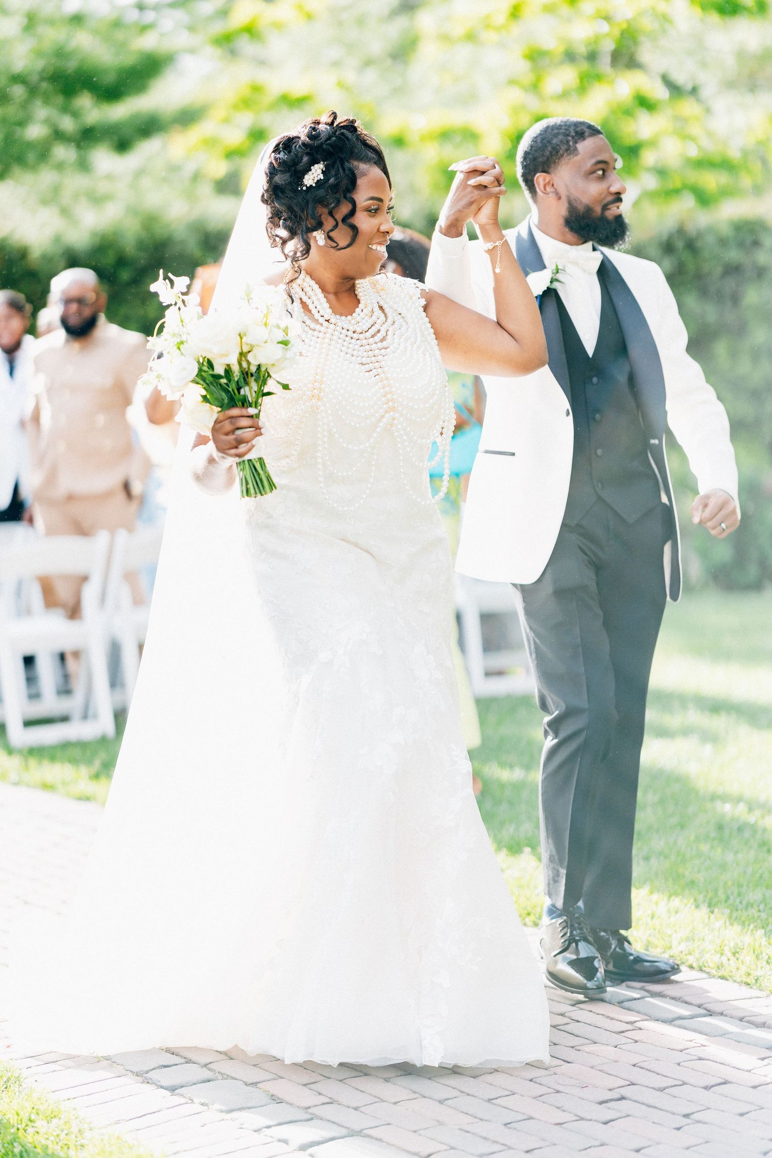 Joyful bride in pearl-embellished gown and groom in white jacket walk back down aisle.