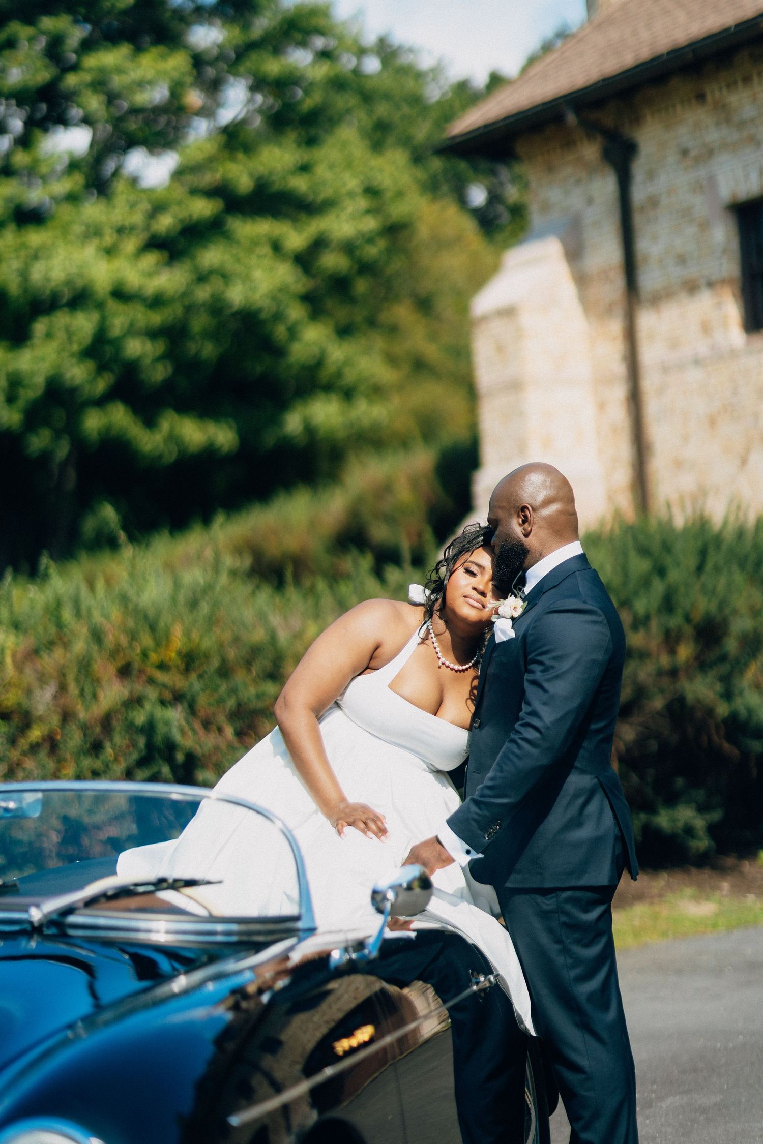 Bride and groom sharing an intimate moment beside a classic black convertible Porsche outdoors.