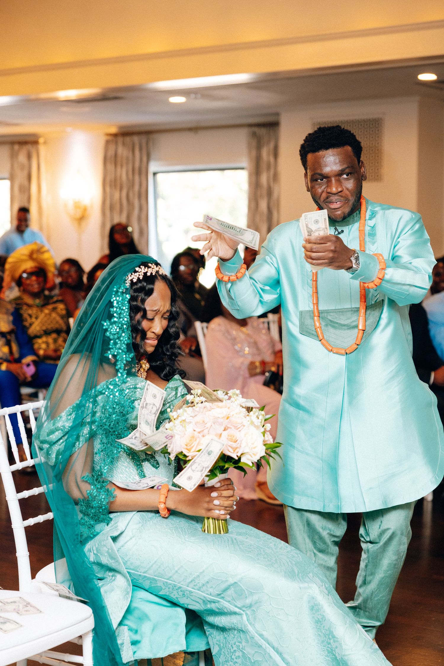 Groom in teal attire showering seated bride with money during traditional wedding celebration.