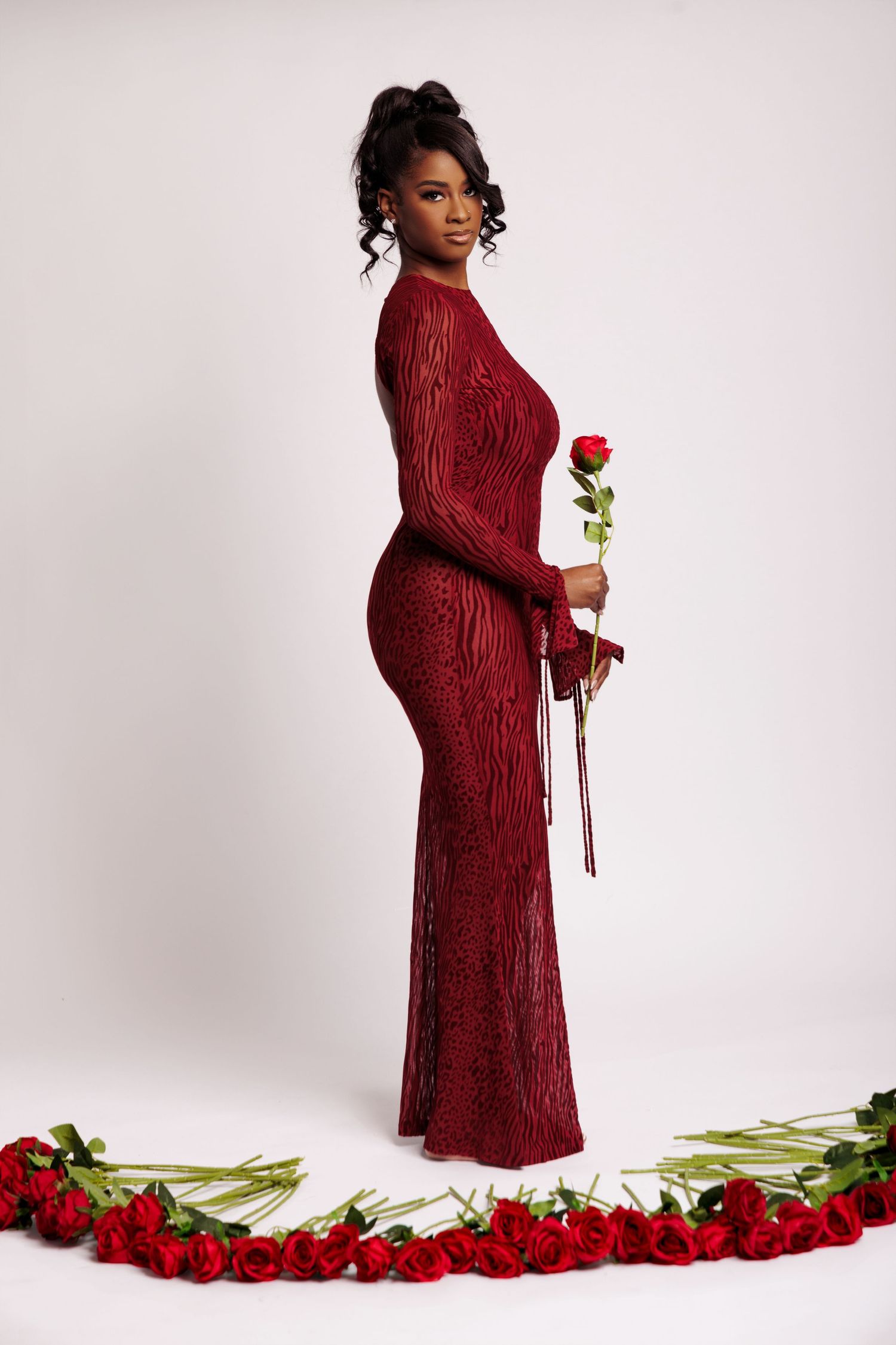 A woman in a red sequin gown holds a rose, surrounded by red roses on a white background.