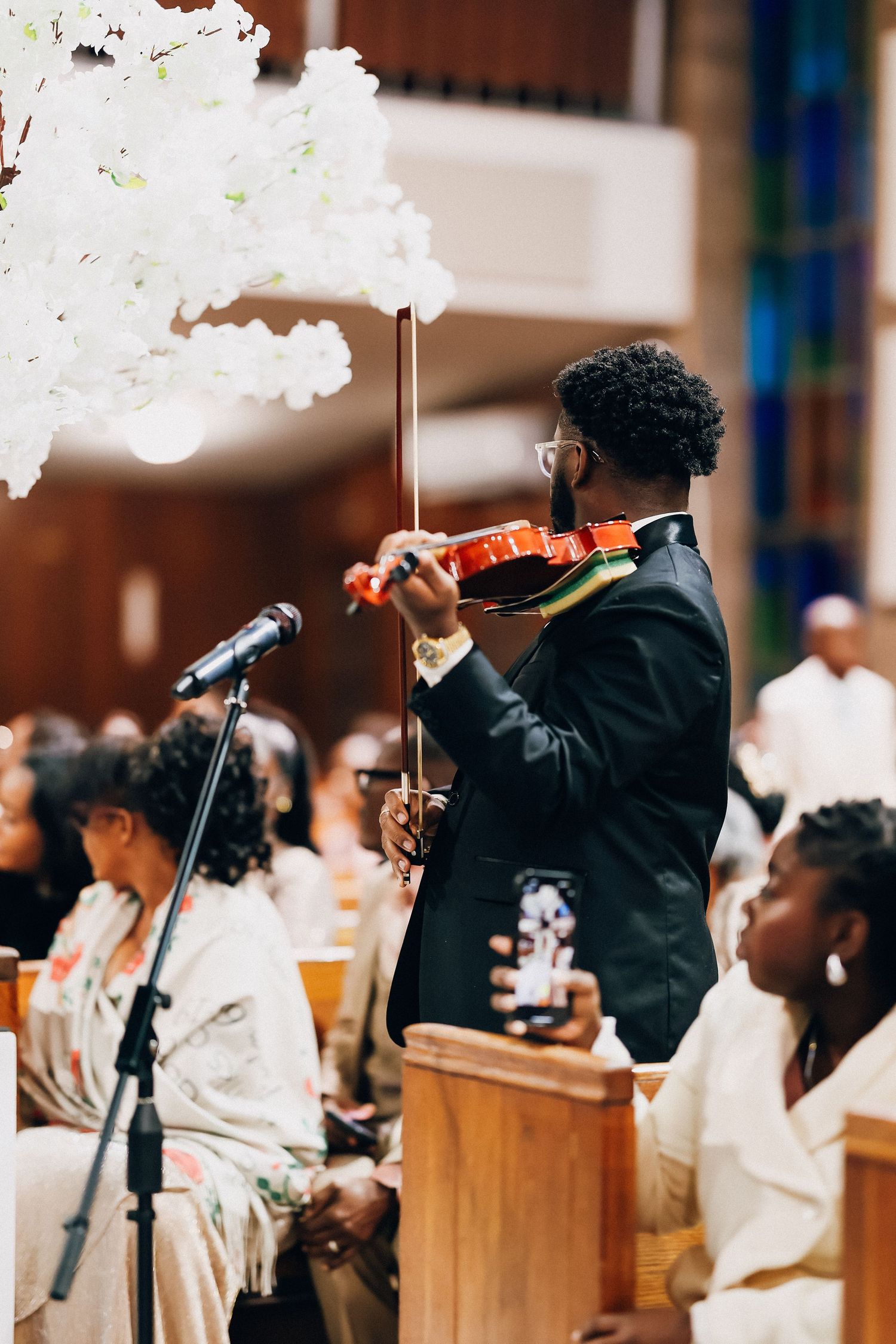 Violinist in a suit performing at an elegant church wedding ceremony with white floral decorations.