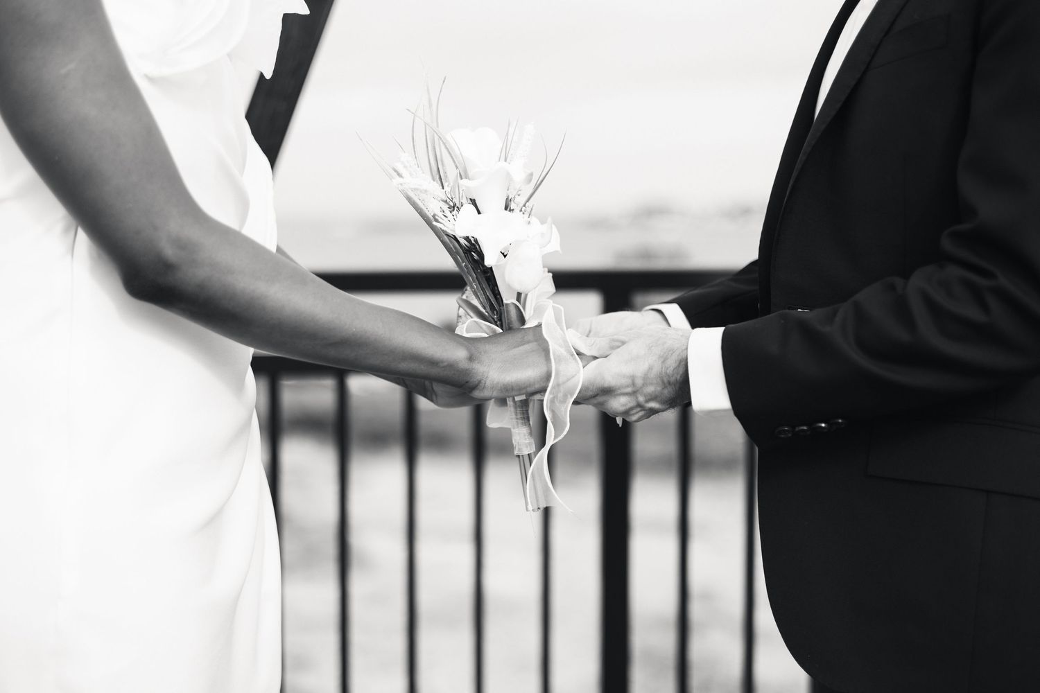 Black and white photo of a bride and groom holding a white floral bouquet during a wedding ceremony.