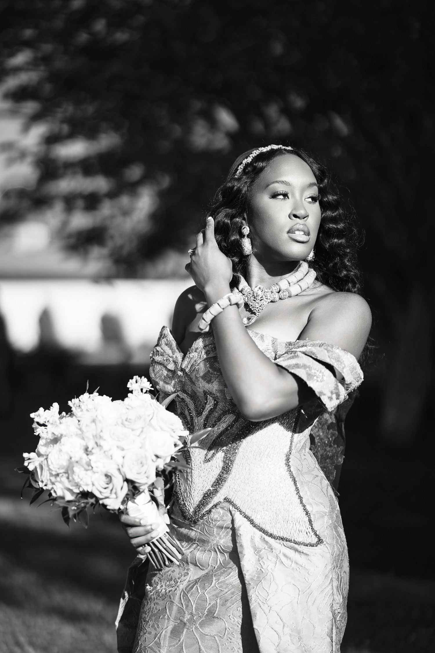Black and white portrait of African bride in ornate gown holding bouquet.