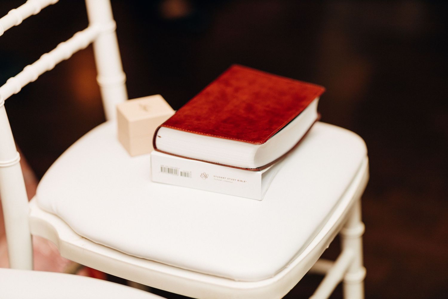 Red velvet Bible and prayer book on white chiavari chair at wedding ceremony.