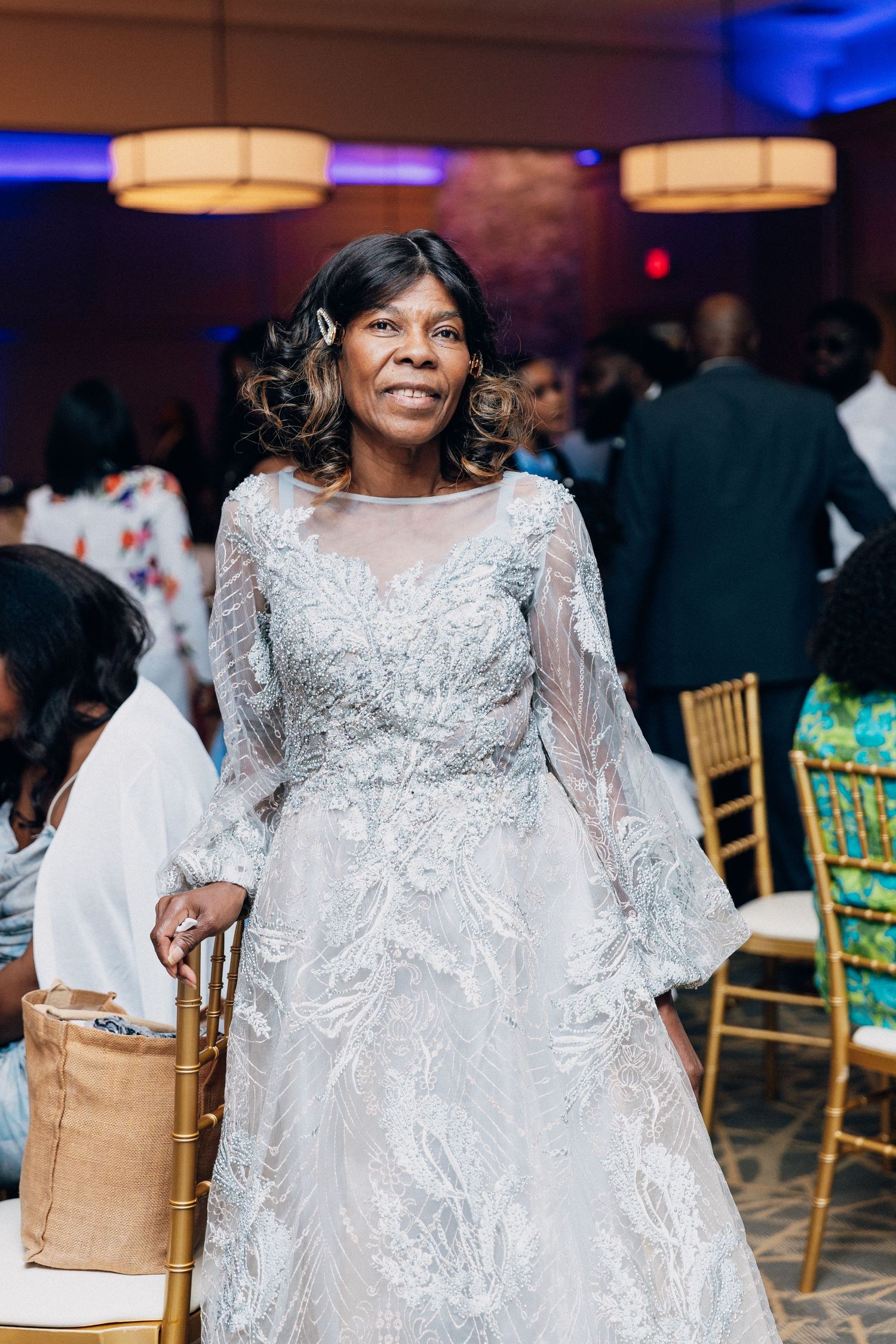 Elegant woman in silver beaded gown smiling at a wedding reception with gold chiavari chairs.