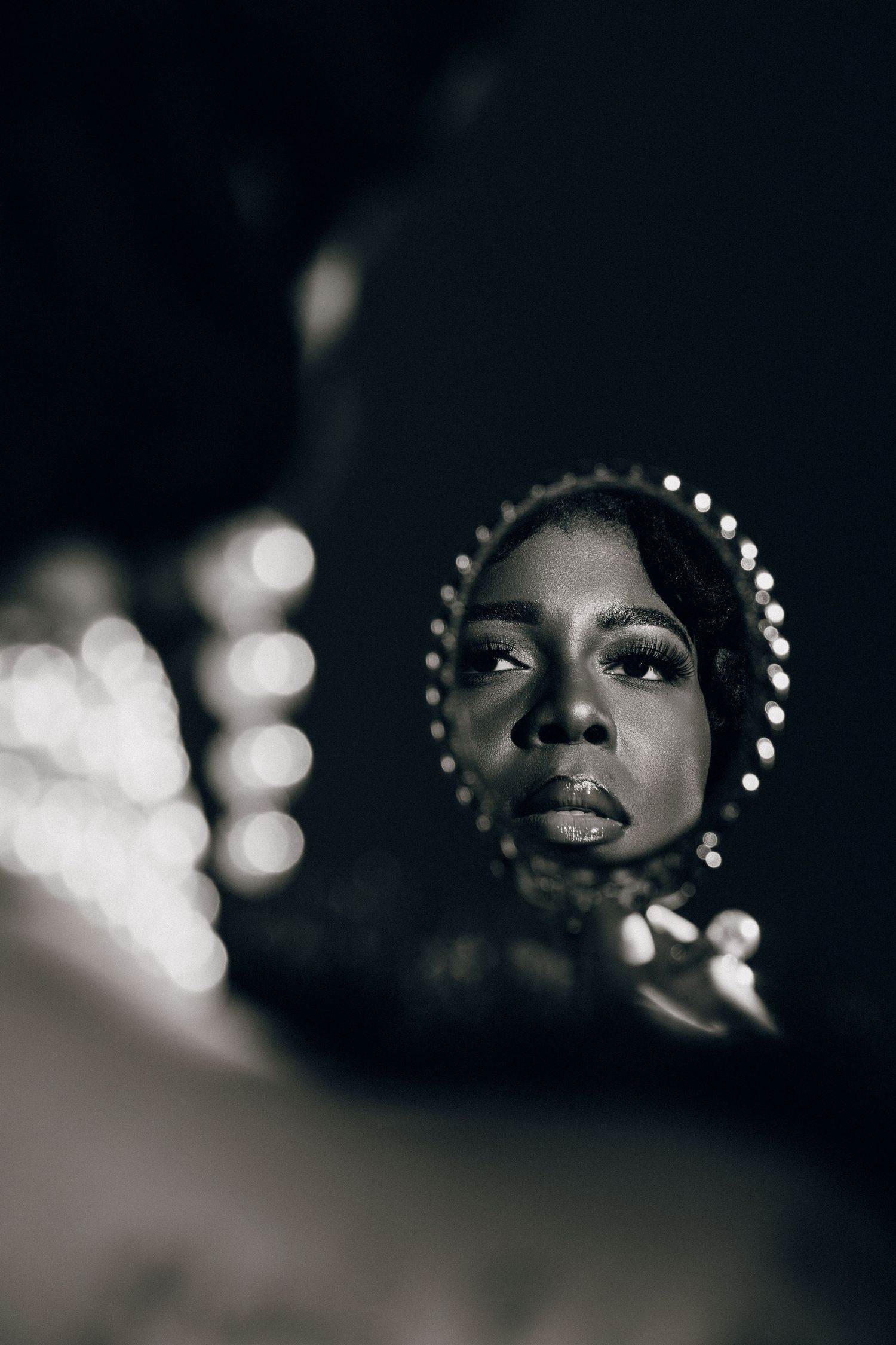 Black and white portrait of a woman with pearl headpiece reflected in a mirror, dramatic lighting.