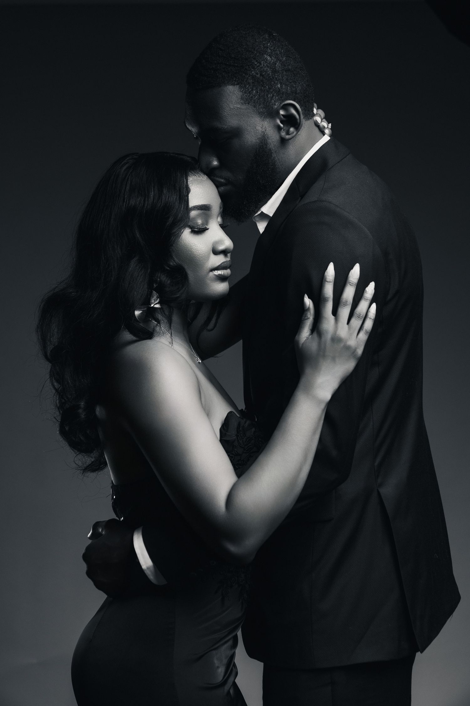 Black and white photo of an elegant couple embracing, woman in evening dress, man in suit, studio portrait.