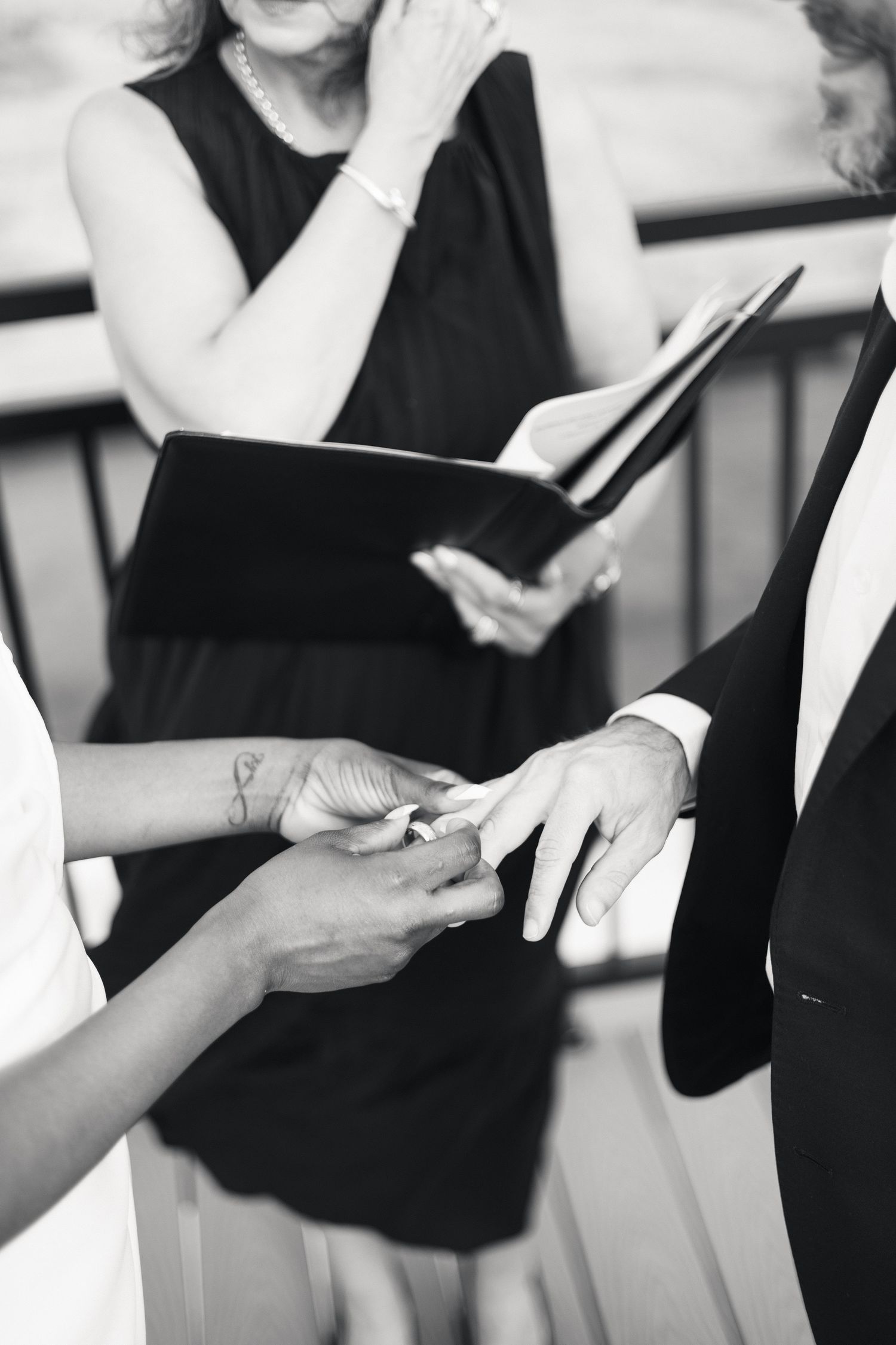 Black and white photo of a bride placing a wedding ring on groom's finger during ceremony.