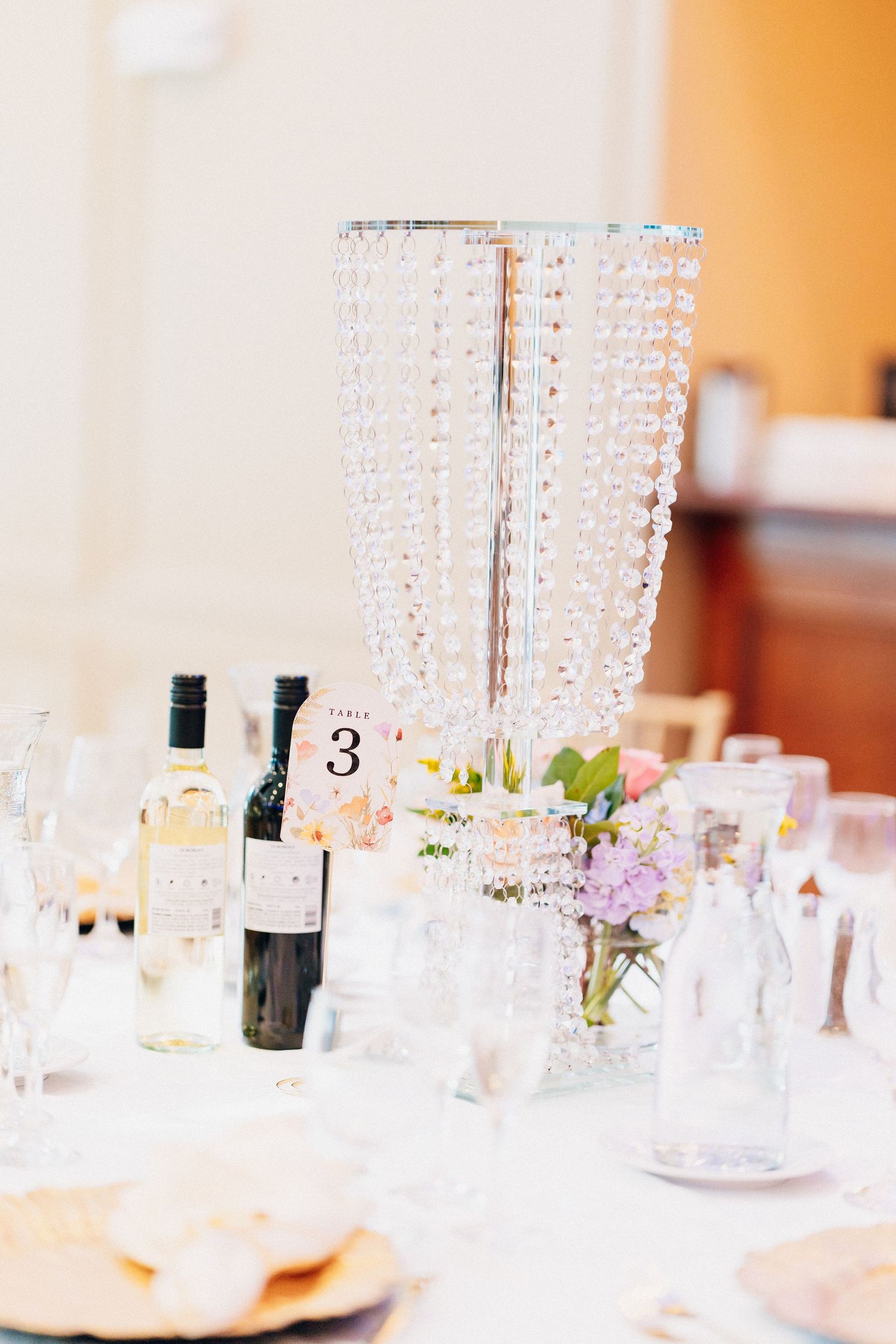 Crystal beaded centerpiece on elegant wedding reception table with wine bottles and floral arrangements.