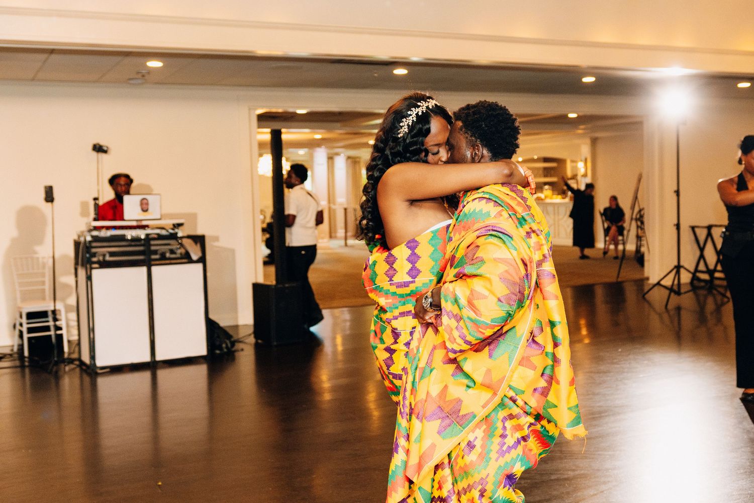 Couple sharing a tender embrace on the dance floor in vibrant traditional Kente cloth wedding attire.