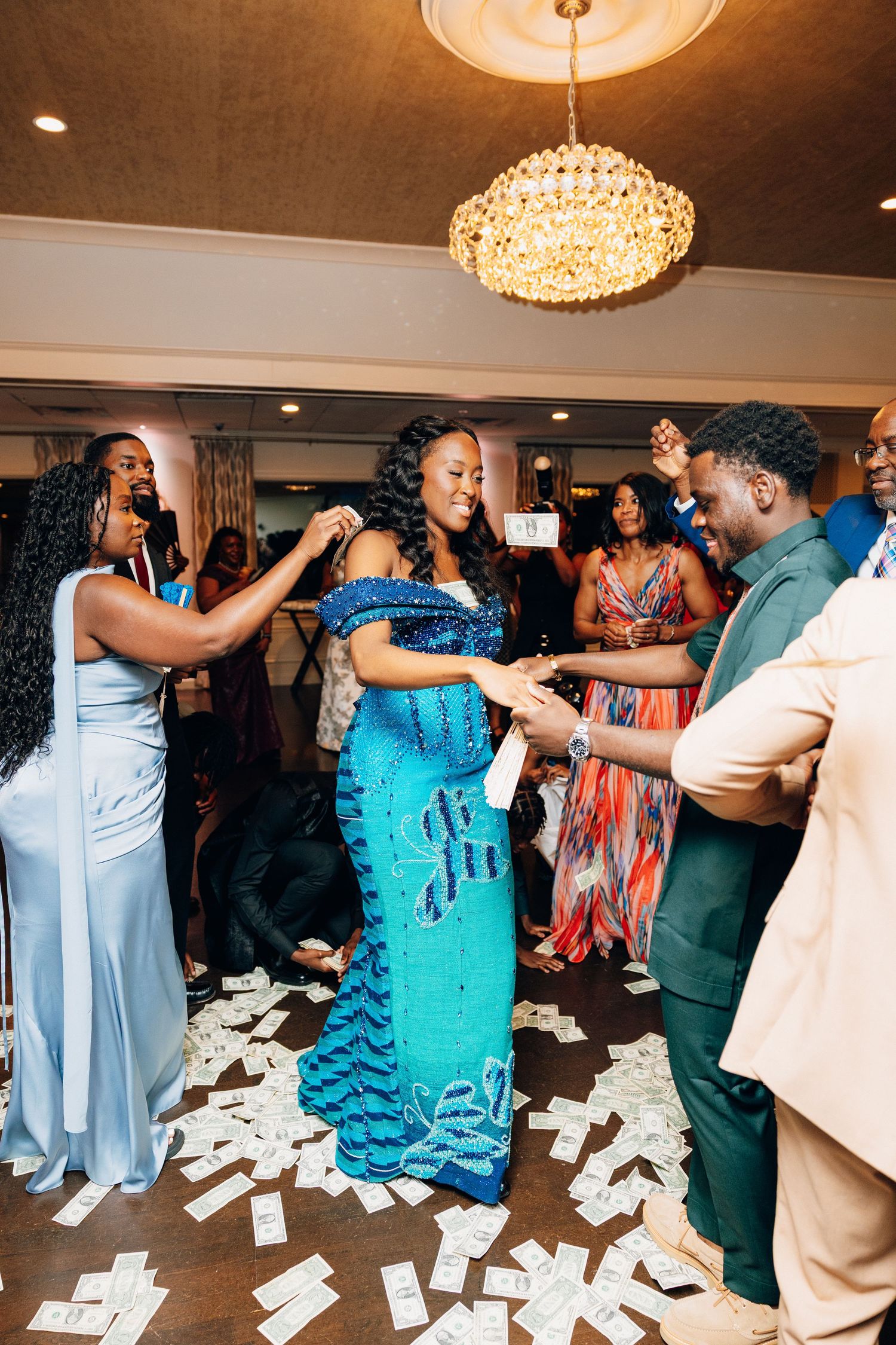 Bride in a stunning blue sequin gown dances as guests spray money at a vibrant wedding reception.
