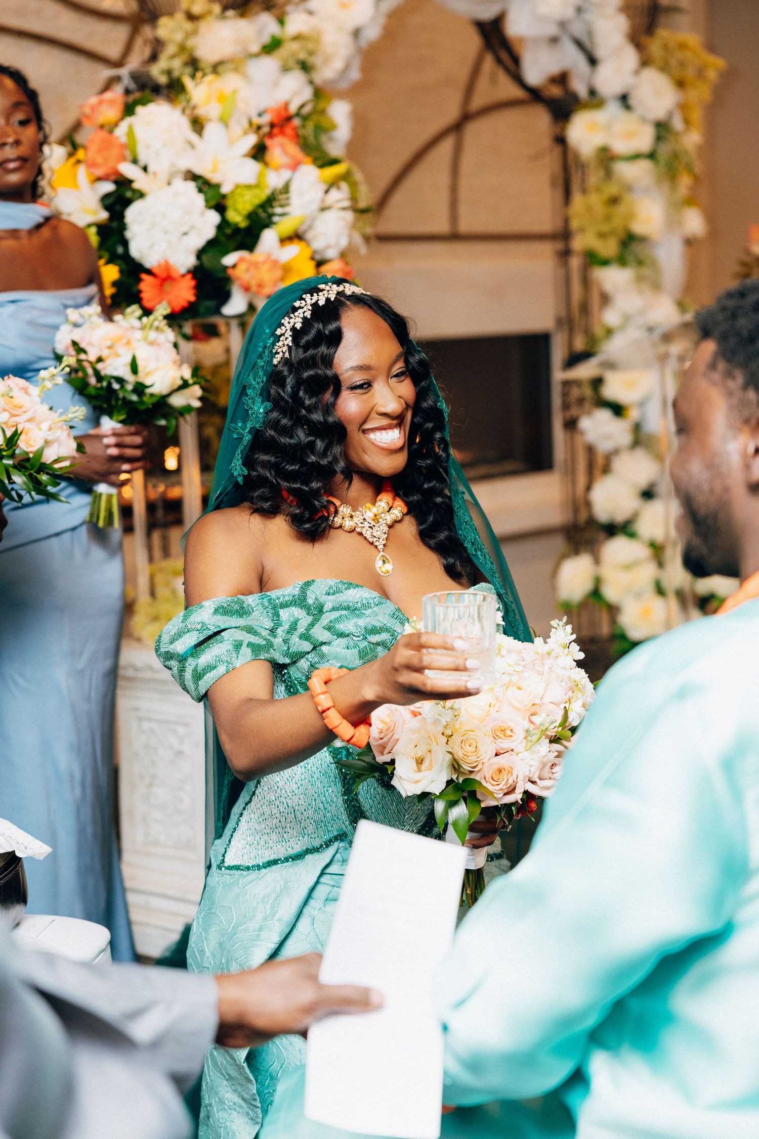 Radiant bride in teal off-shoulder gown smiles while exchanging gifts at traditional African wedding ceremony.