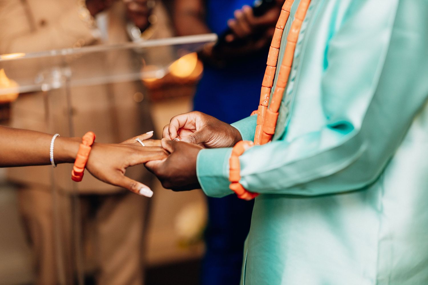 Close-up of a couple exchanging rings during an African wedding ceremony, wearing traditional teal and orange attire.
