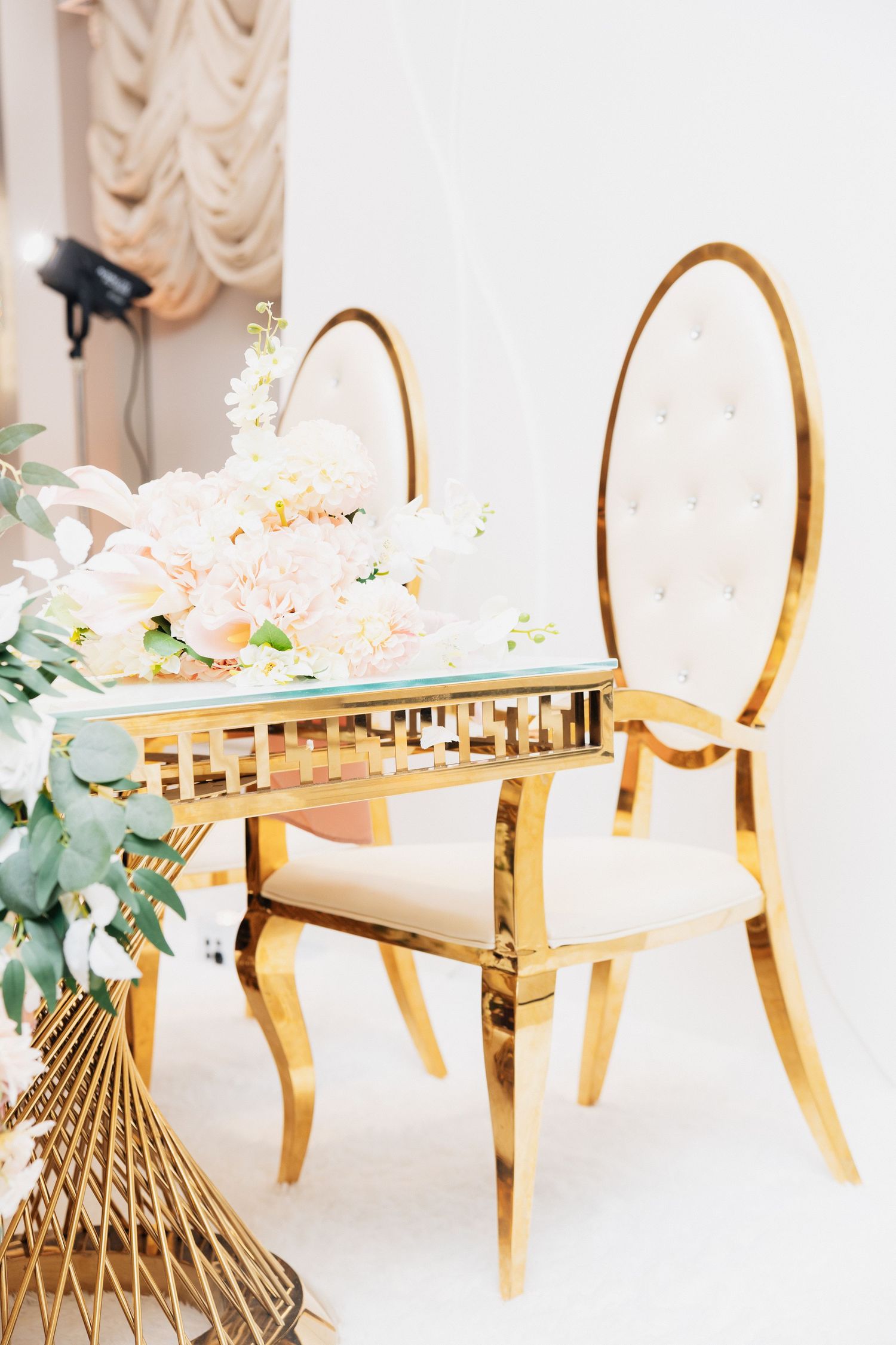 Elegant gold sweetheart table with cream tufted chairs and white floral centerpiece at a luxury wedding venue.