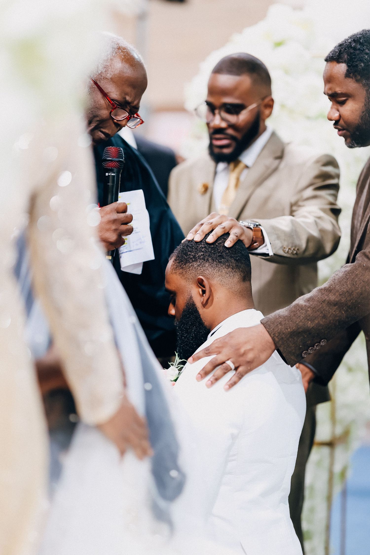 Men laying hands in prayer on a groom during a wedding ceremony.