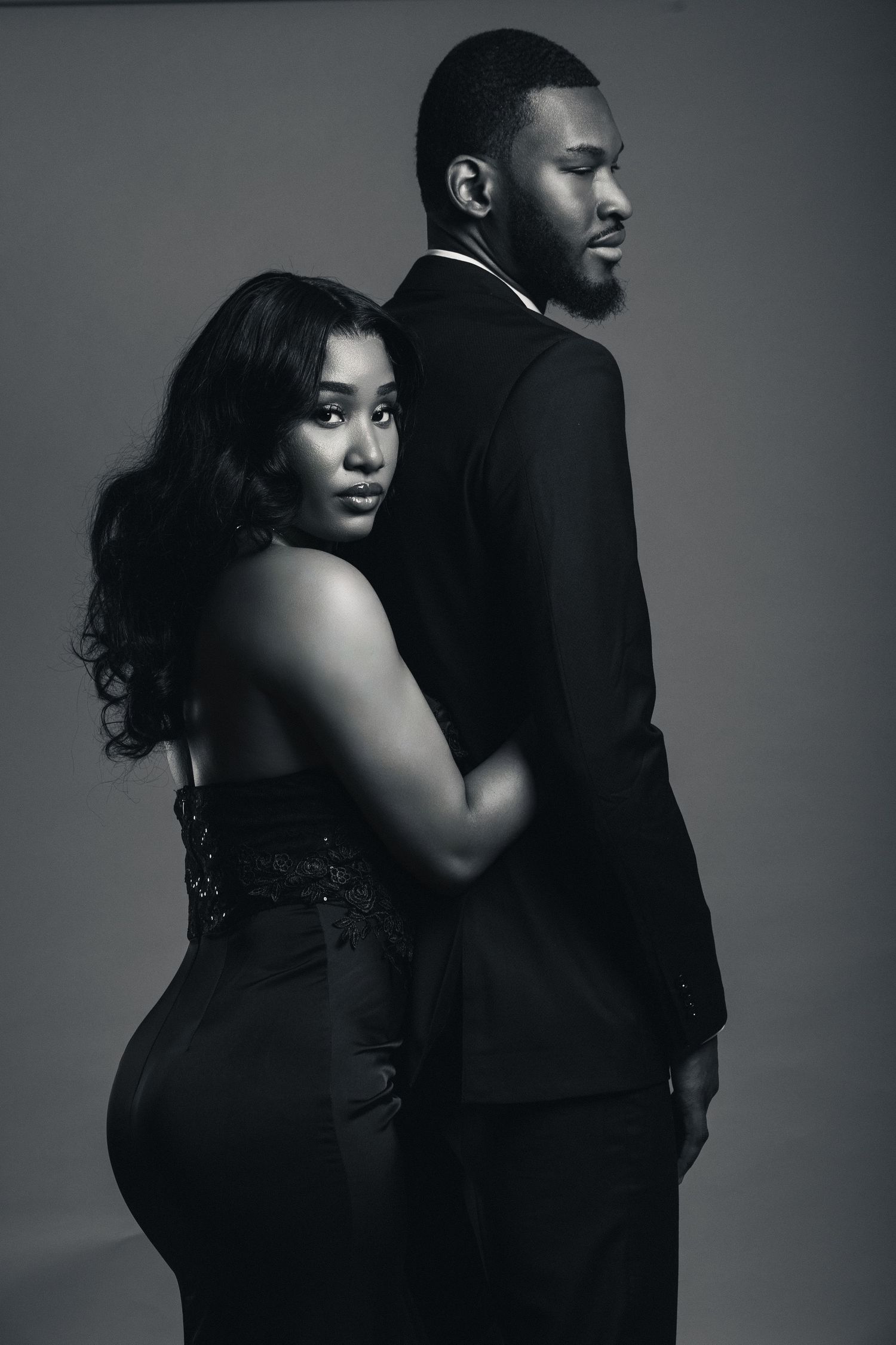 Elegant black and white portrait of a couple in formal attire, woman in strapless gown leaning back on man in suit.