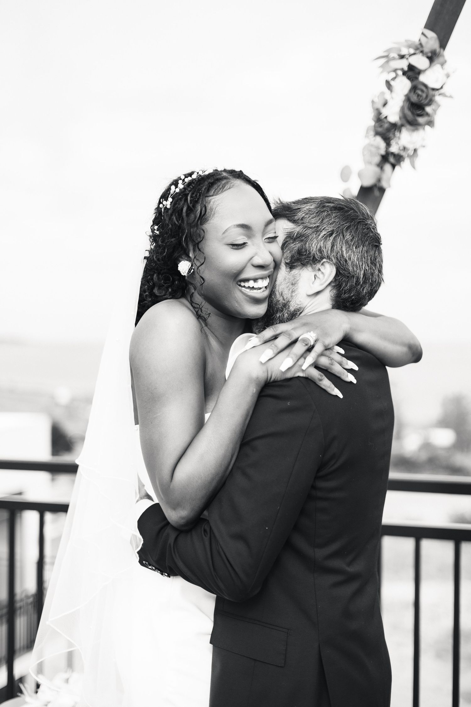 Joyful bride in white gown embraces groom after first kiss during rooftop wedding ceremony.