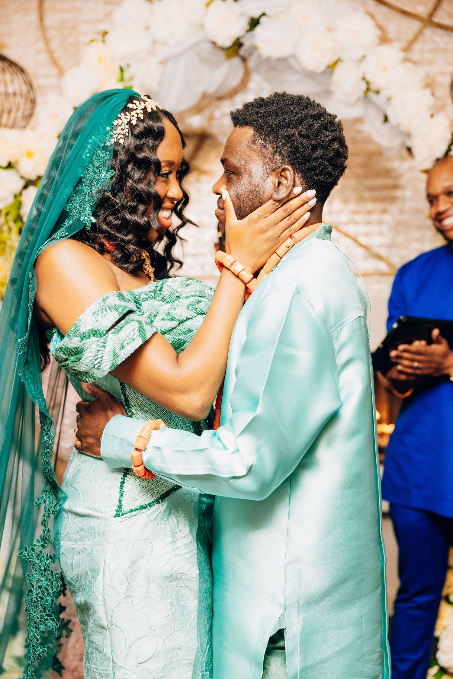 A bride and groom in matching teal outfits share an intimate moment during their traditional African wedding ceremony.