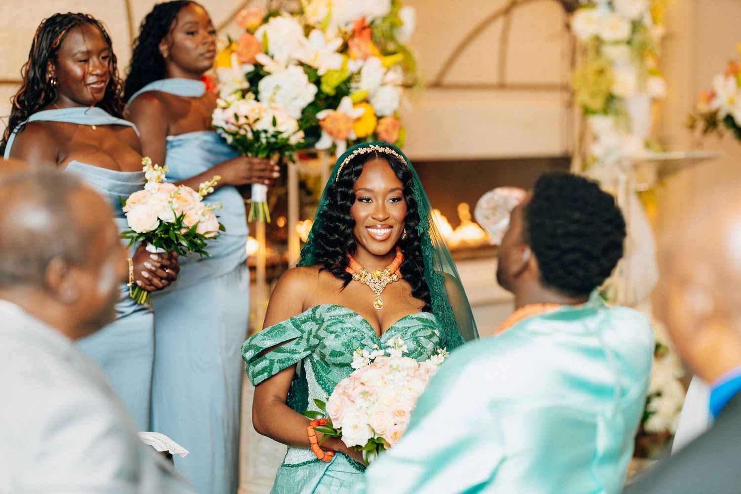 Radiant bride in teal gown walks down aisle past bridesmaids in blue dresses at elegant wedding.
