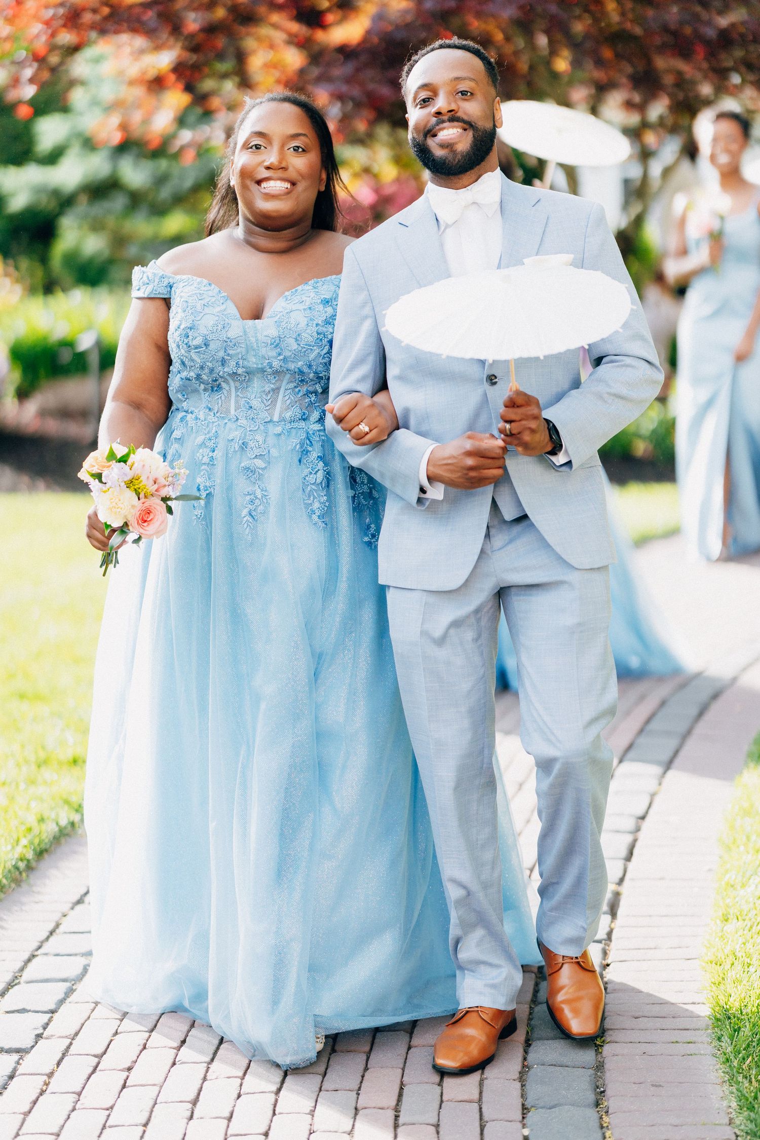Bridesmaid in blue lace gown and groomsman in light blue suit pose with parasol.