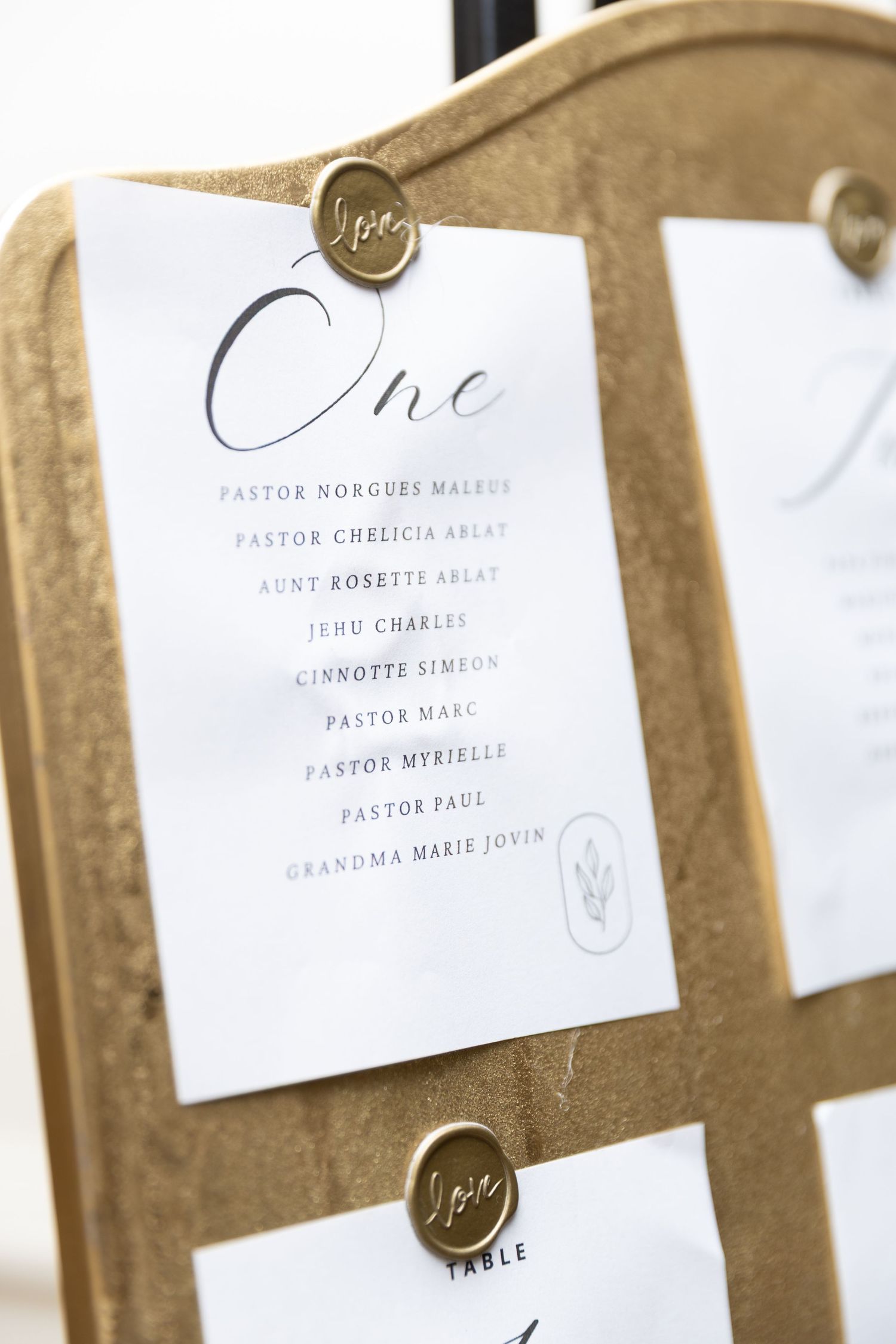 Gold easel displaying elegant wedding seating chart cards with wax seals for table number one.