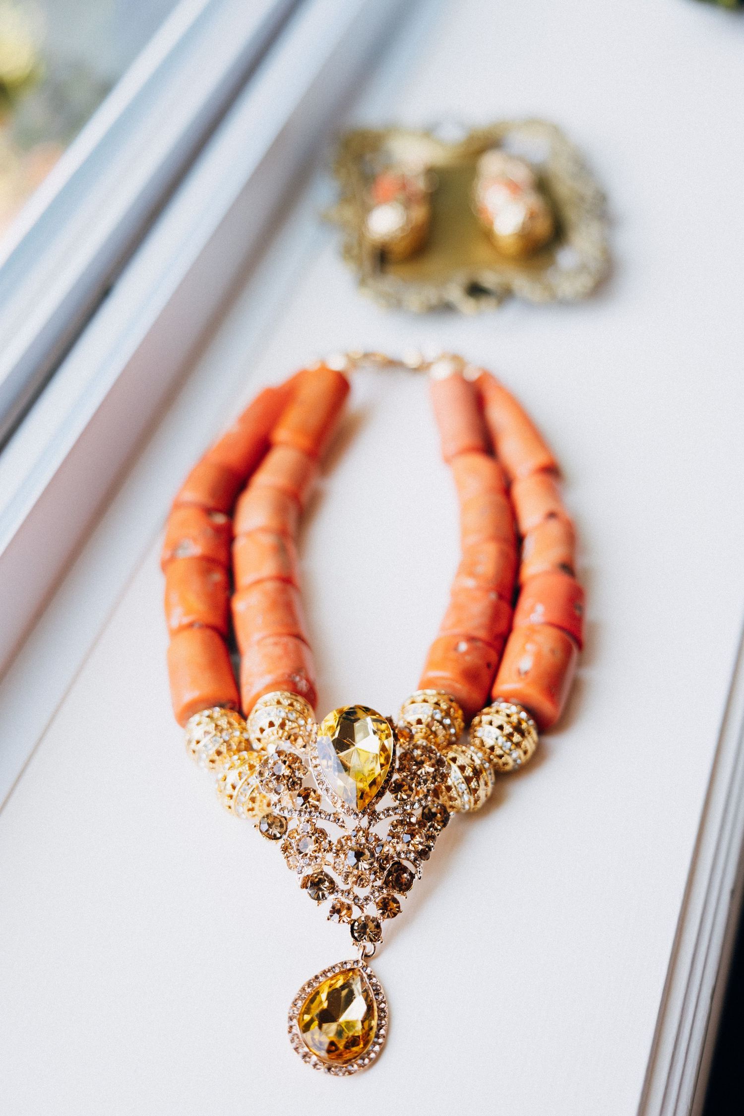 Elegant coral beaded bridal necklace with gold filigree and yellow gemstone pendant displayed on white surface.