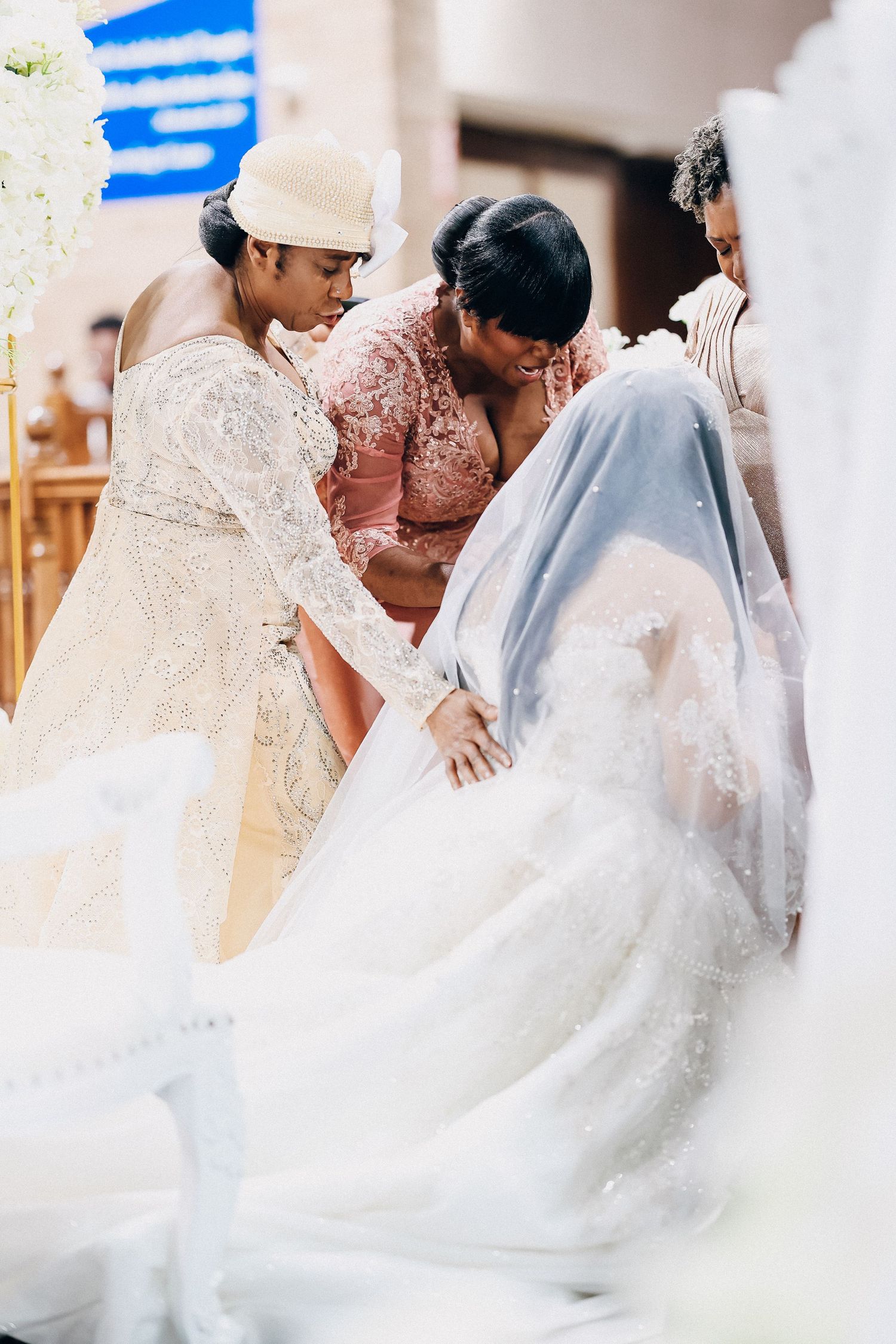 Bridesmaids helping bride with her white lace wedding gown inside a church ceremony.