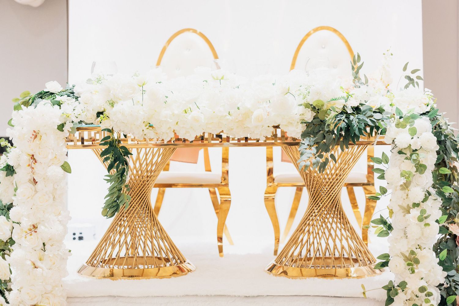 Gold geometric chairs and a sweetheart table adorned with lush white floral arrangements at an elegant wedding reception.