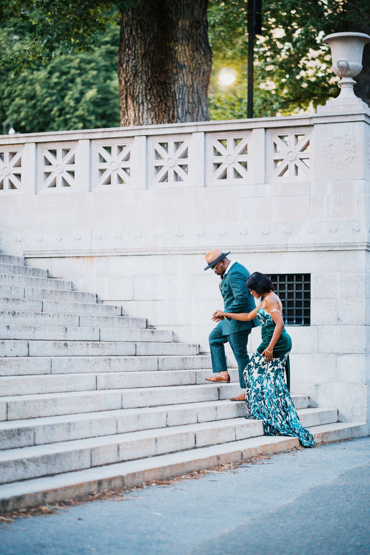 Couple in formal attire walking down grand white marble steps at sunset.