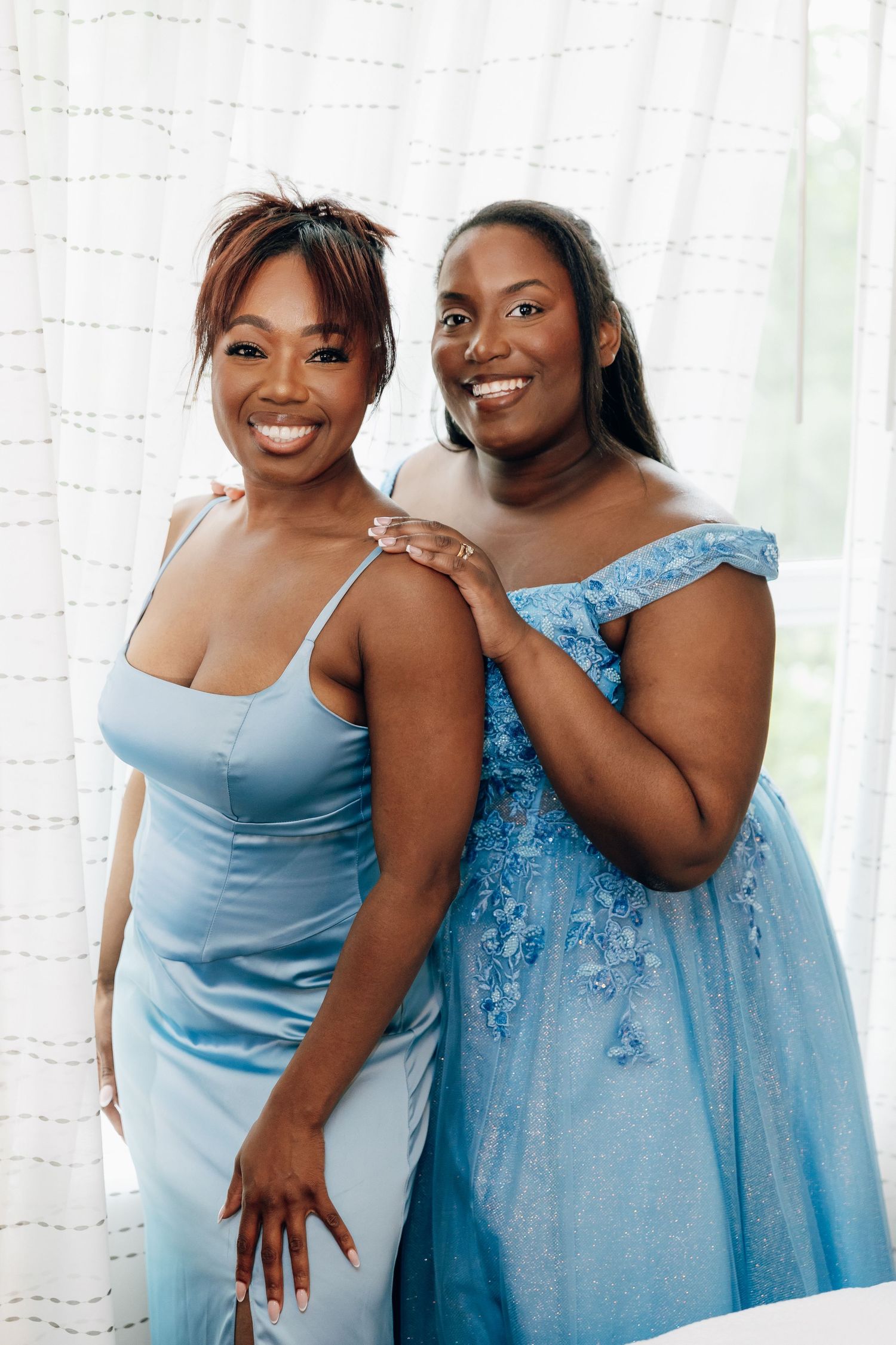 Two Black bridesmaids smiling together wearing matching light blue dresses before wedding ceremony.