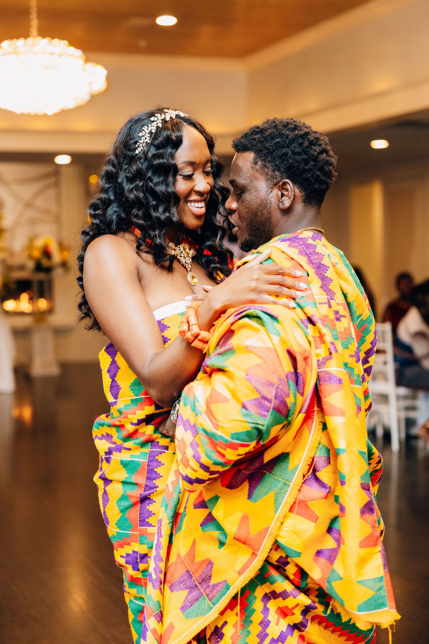 Couple dancing in vibrant African kente cloth outfits at a wedding reception.