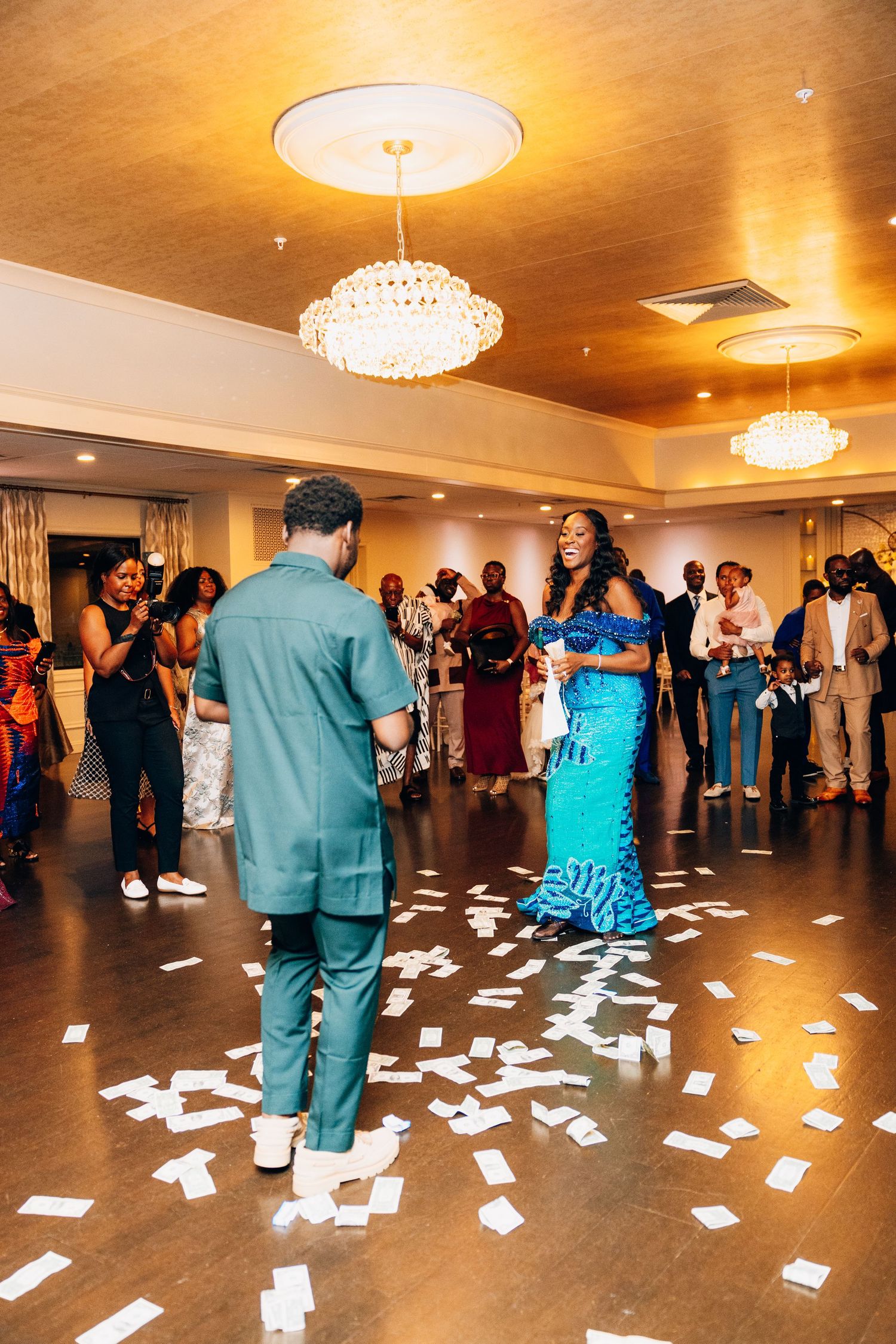 Bride in blue mermaid gown and groom in teal suit share first dance on confetti-covered ballroom floor.