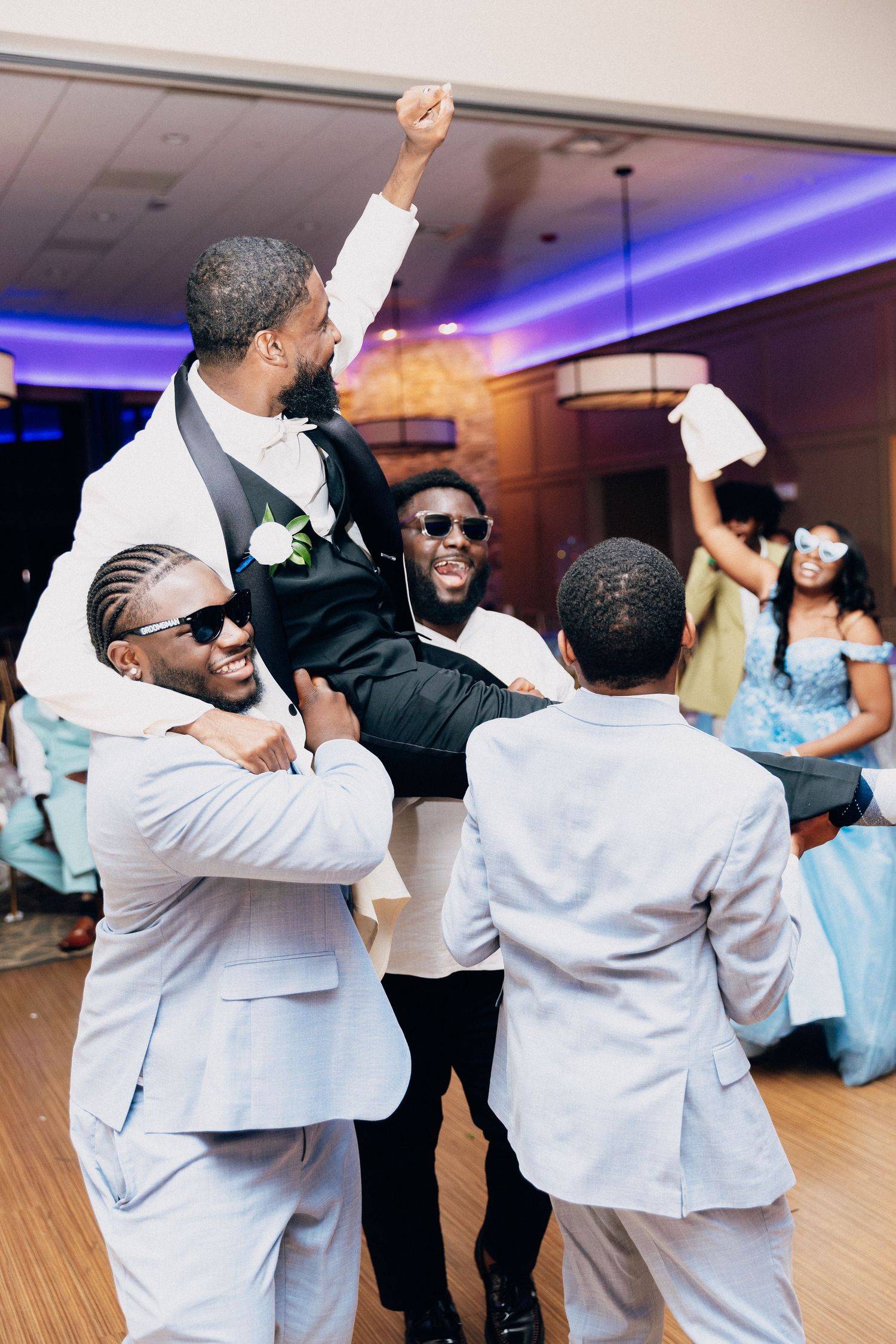 Groomsmen celebrate by lifting the groom on their shoulders during a lively wedding reception dance.
