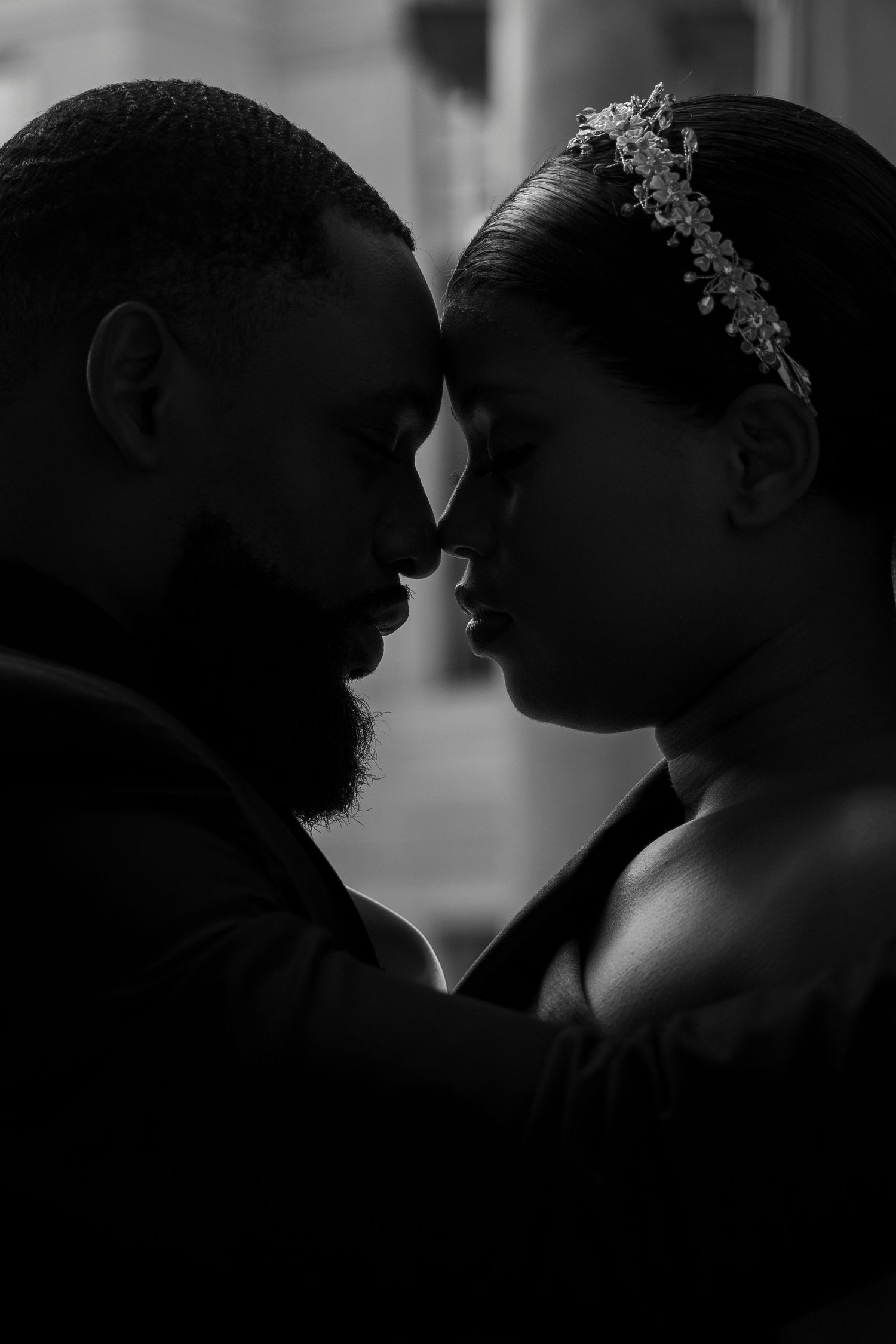 Black and white silhouette of a couple with foreheads touching, bride wearing floral headpiece in romantic portrait.