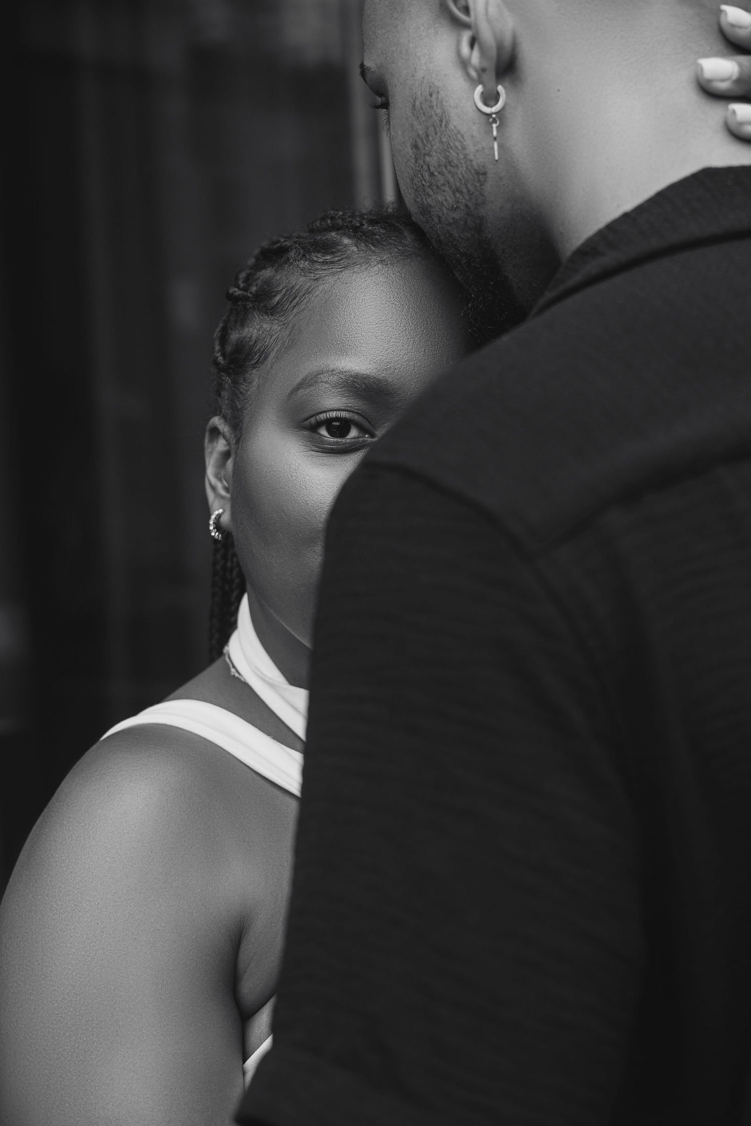 Black and white portrait of a woman peeking behind a man, showcasing intimacy and emotion in a dramatic close-up shot.