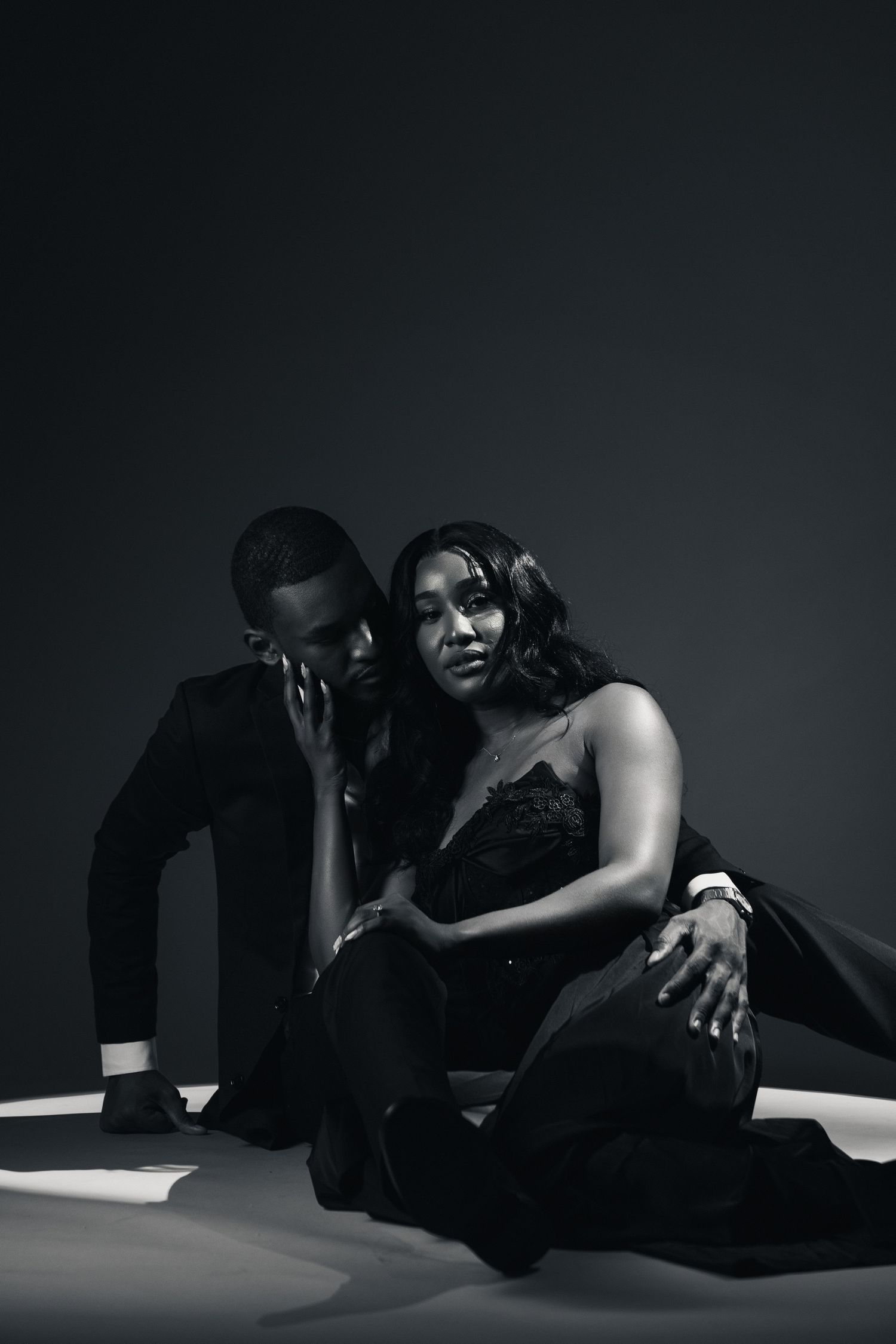 Black and white photo of an elegant couple in formal attire posing dramatically in a spotlight on a dark background.
