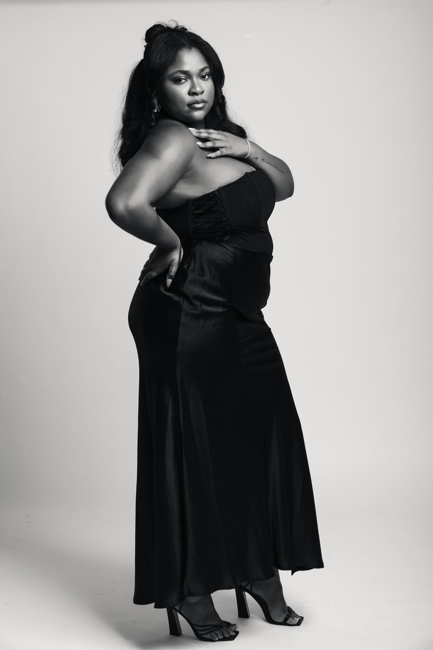 Black and white photo of a woman in an elegant strapless black gown posing confidently in heels.