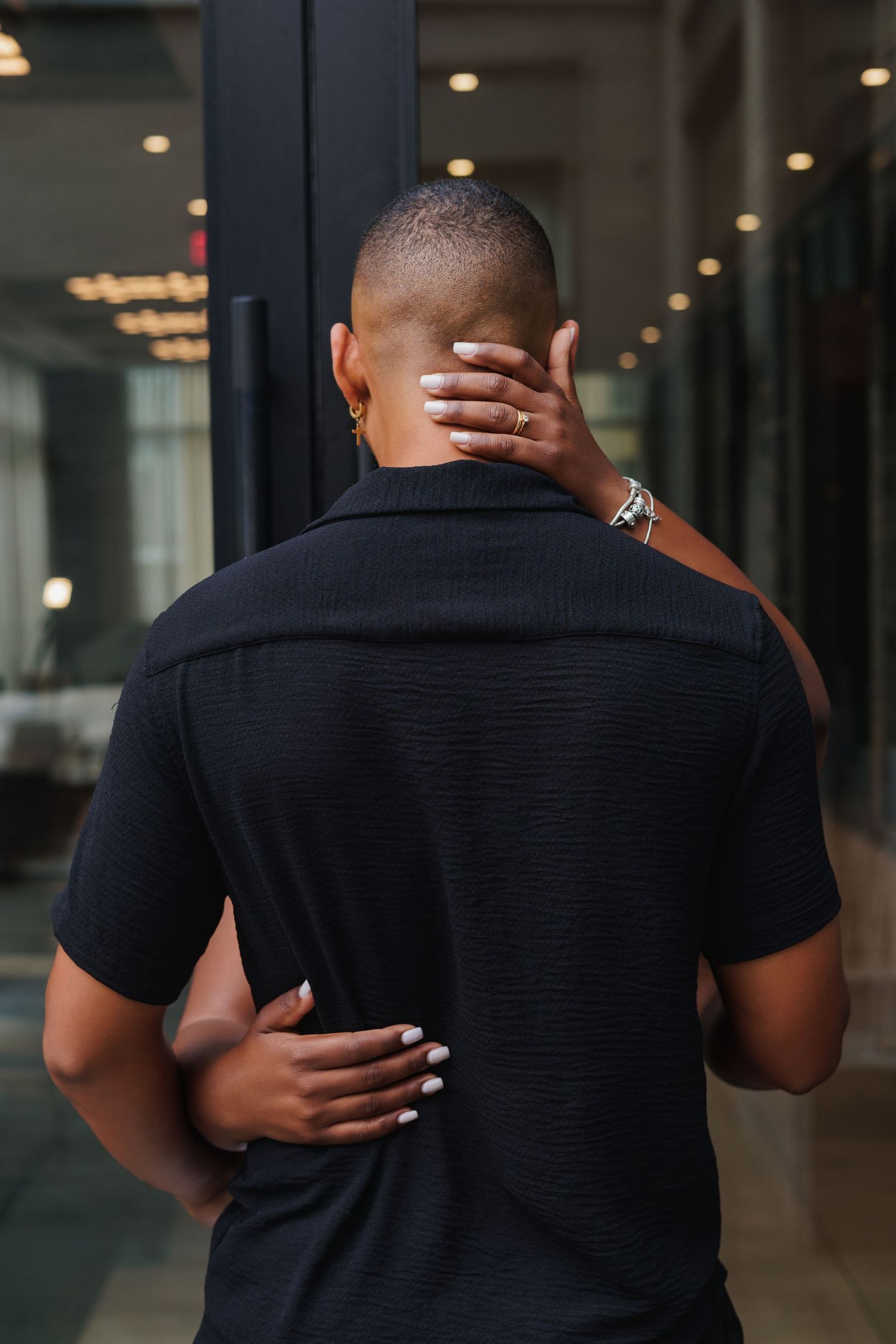 A person in a black polo shirt seen from behind with someone's hands resting on their neck and lower back.